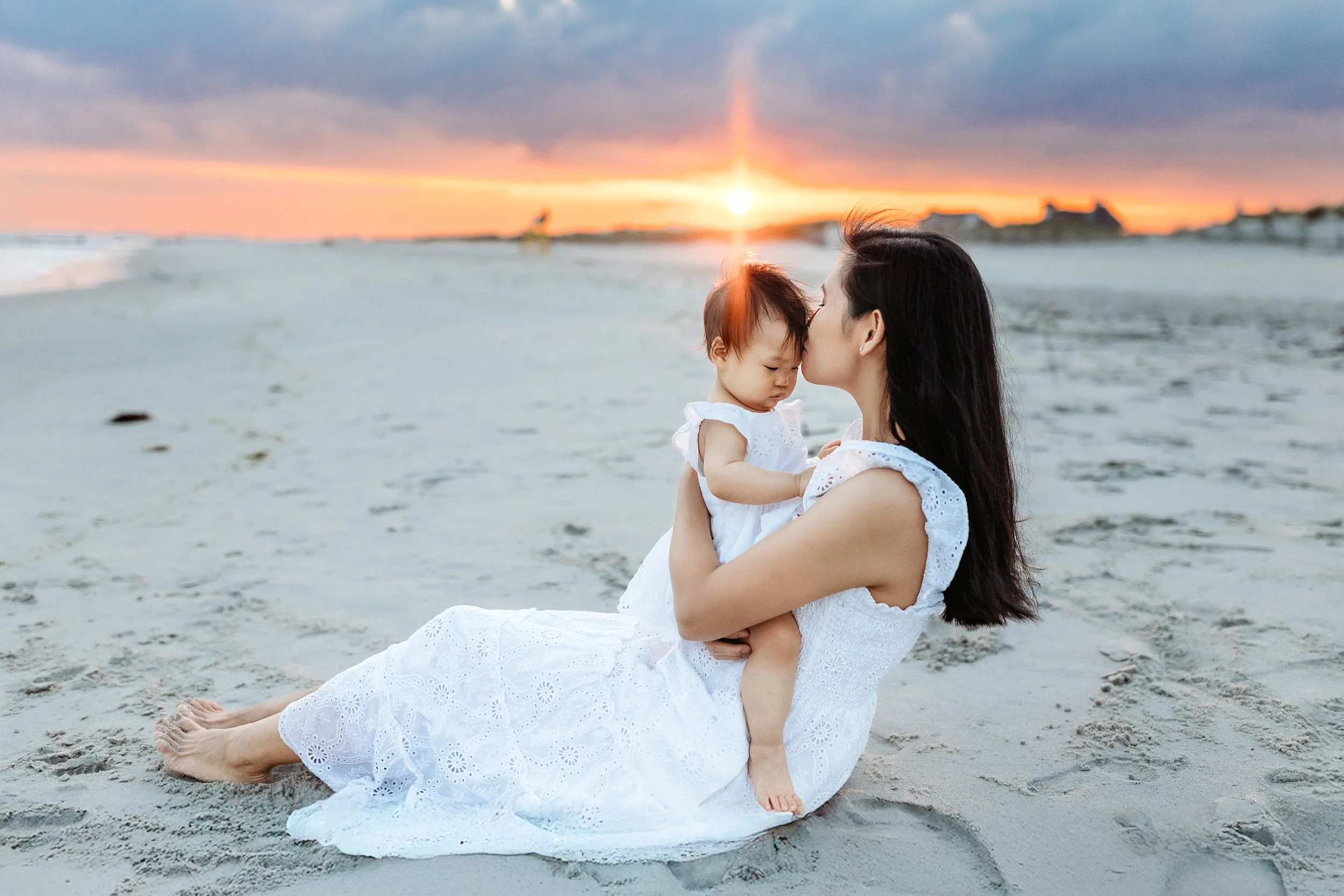 mother kissing baby on the beach at sunset