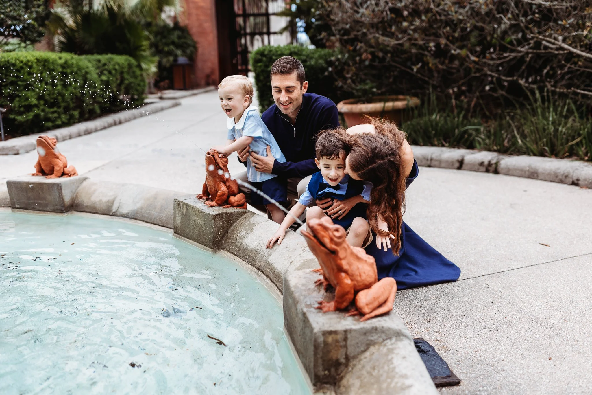 family laughing and playing and hugging toddler boys by a fountain at Flagler college