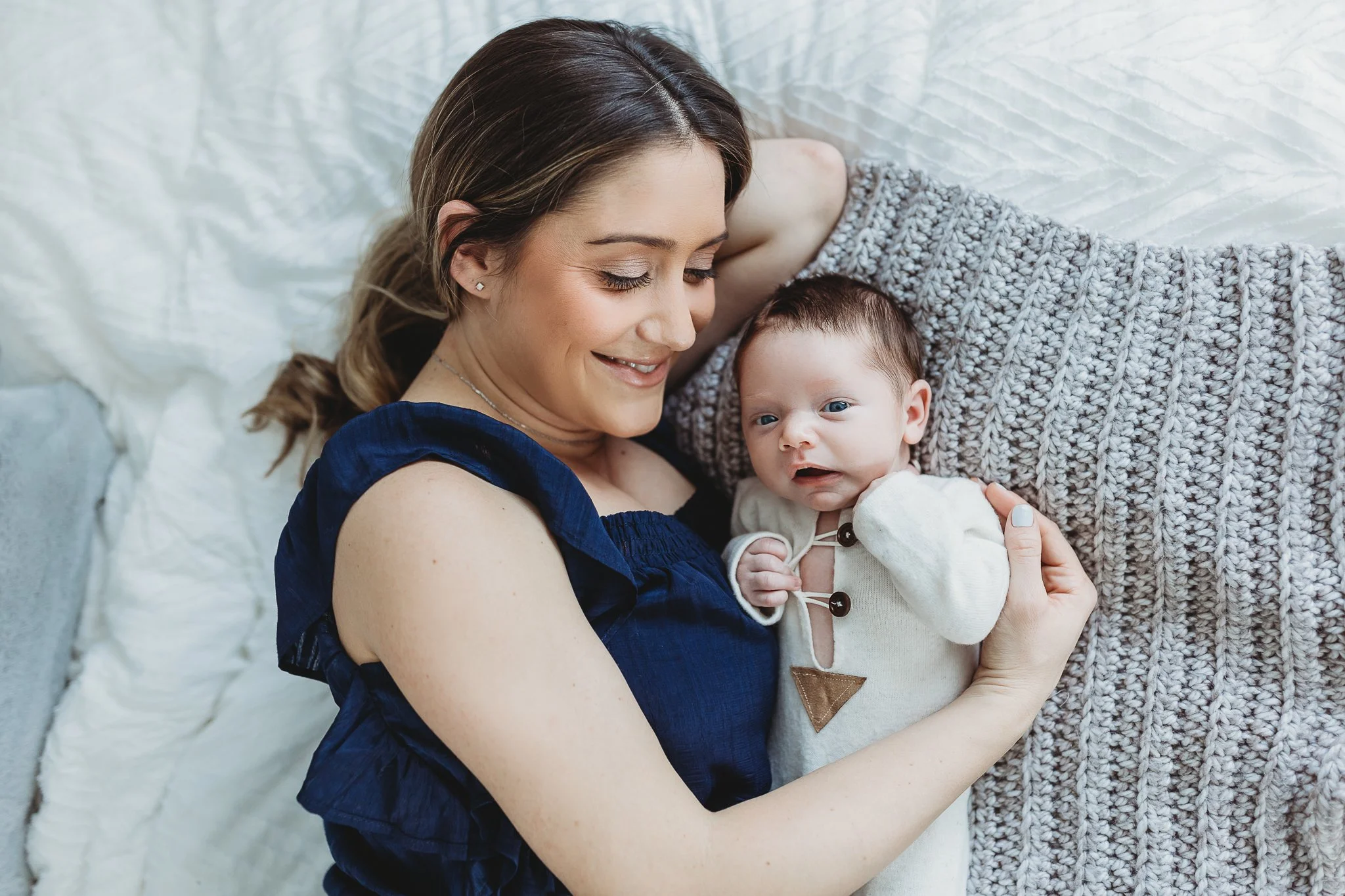 mom in navy blue dress laying in a bed looking at her baby next to her