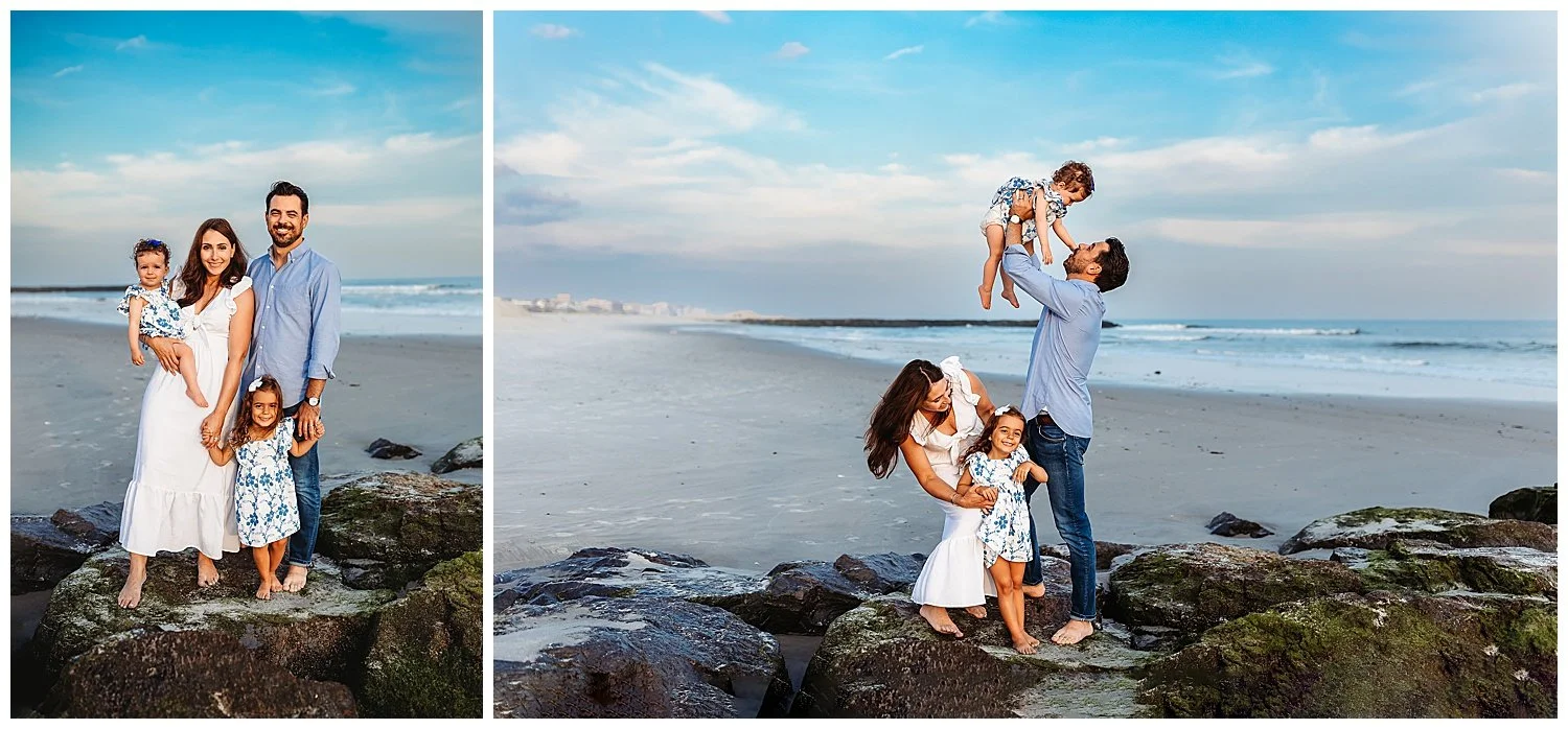 family on a jetty with a bright blue cloudy sky behind them at the beach dad is picking up baby girl in air mom crouched down embracing toddler girl