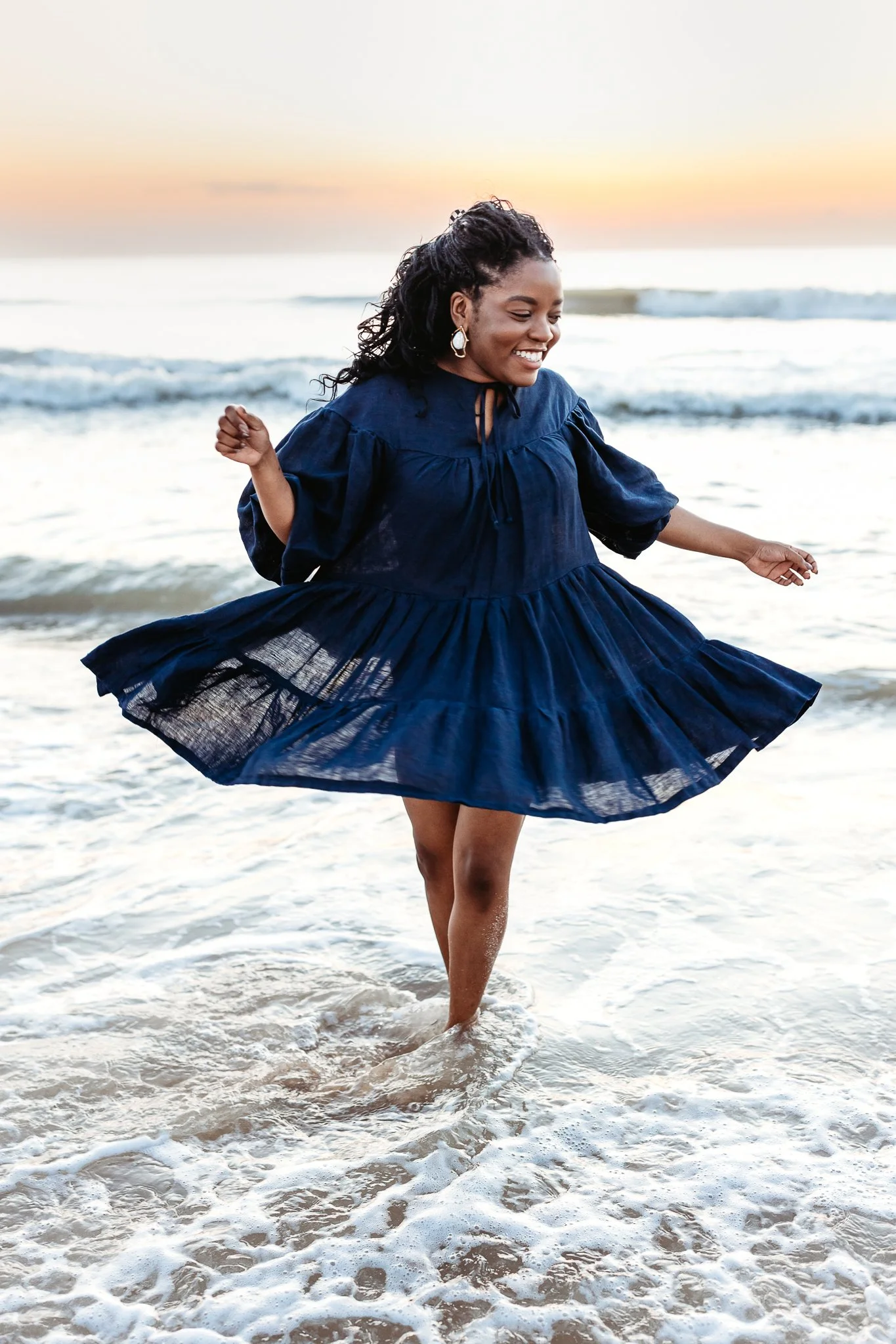 adult daughter twirling in the ocean at sunrise and laughing