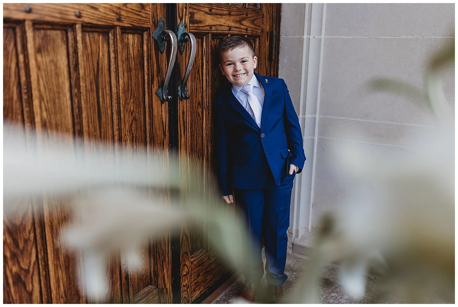 boy in navy suit leaning against church door on communion day