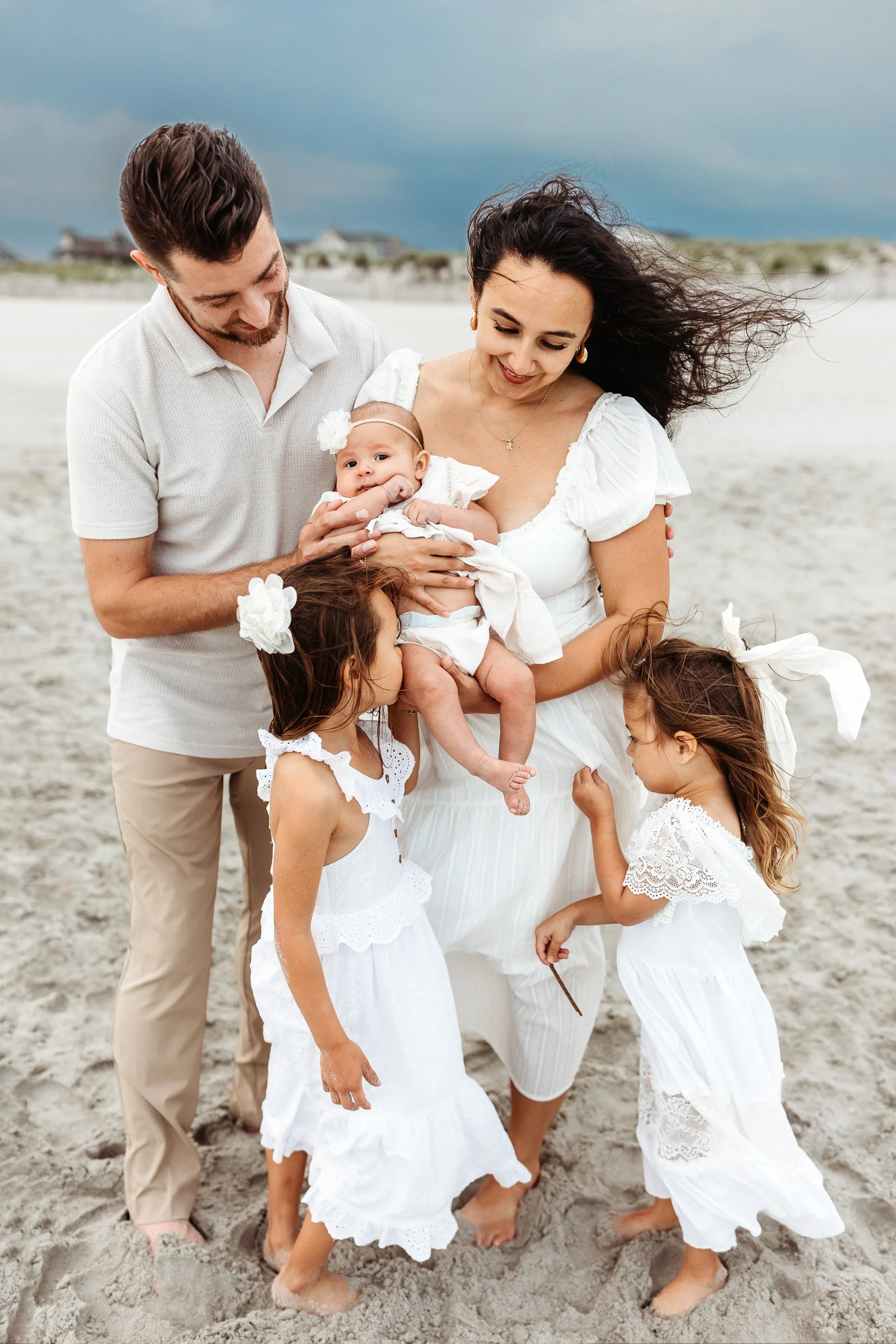portrait of a family looking at a baby or kissing the abby on the beach with a cloudy grey sky