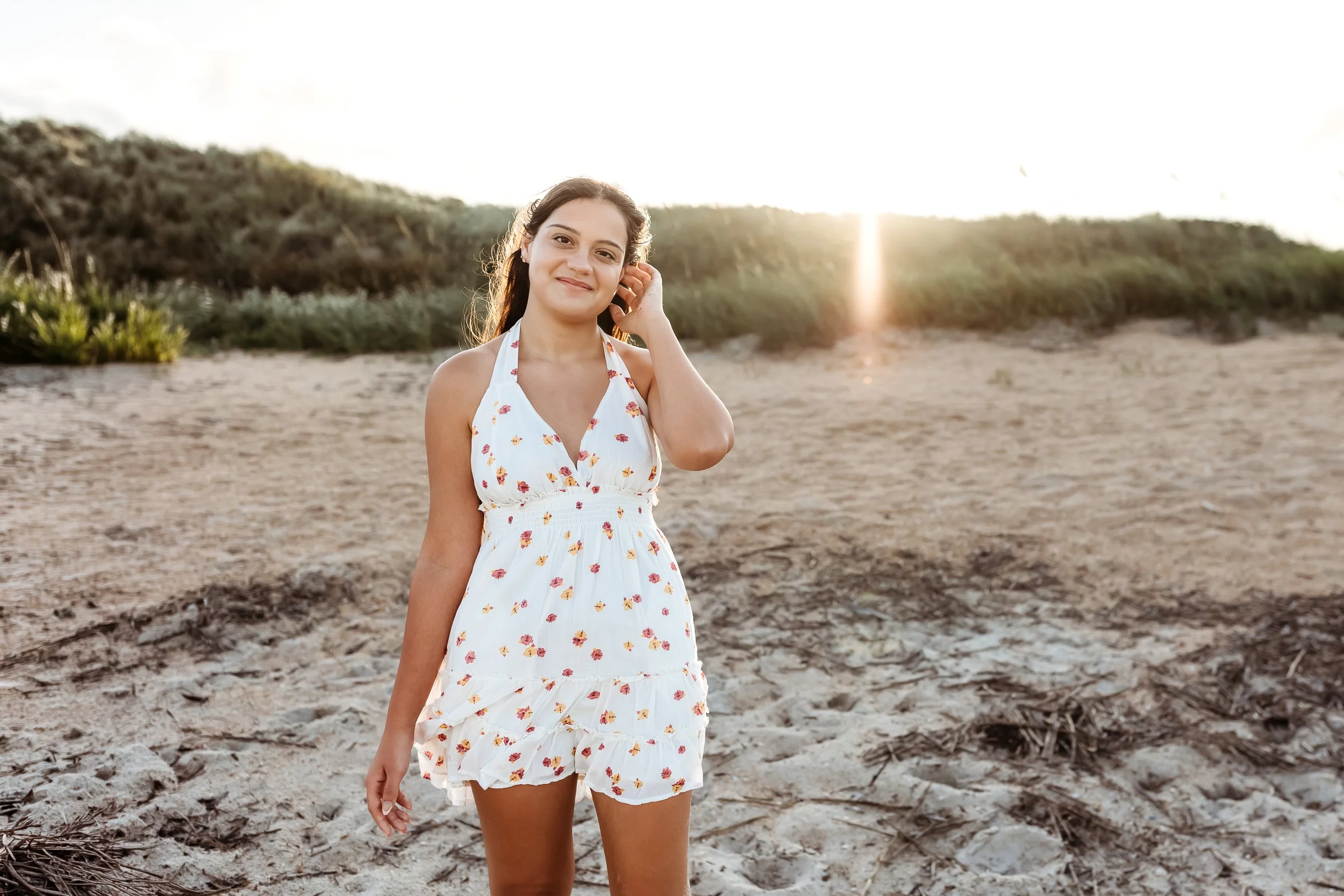 girl taking hair behind ear and she is standing on a dune with golden sunset light streaming over