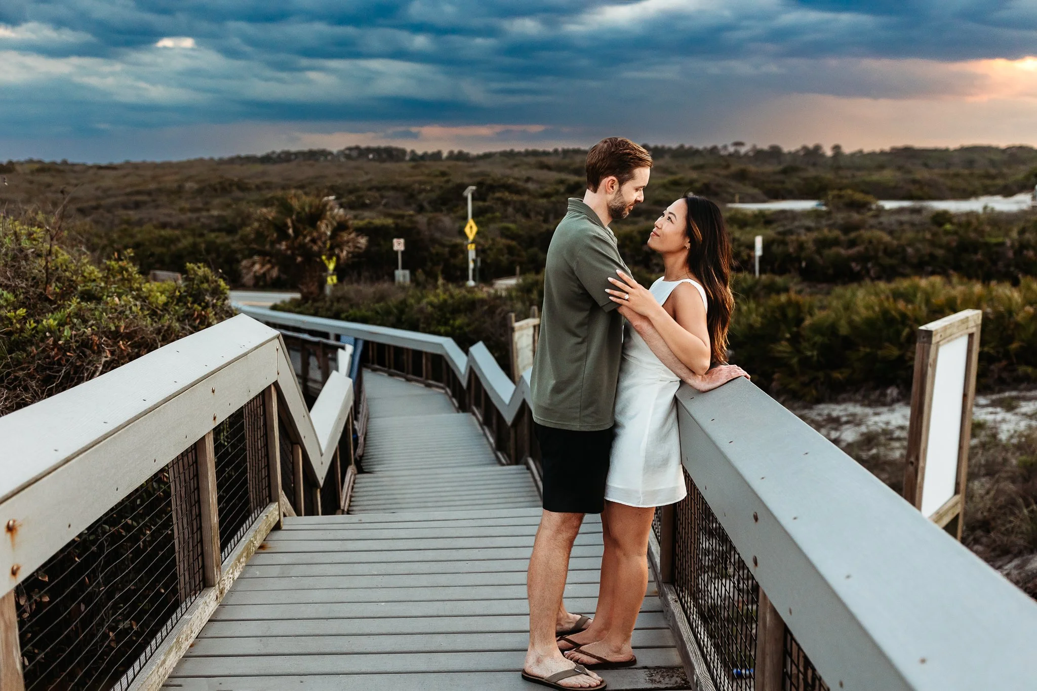couple leaning up against entrance to guana preserve with a pink and blue cloudy sky at sunset