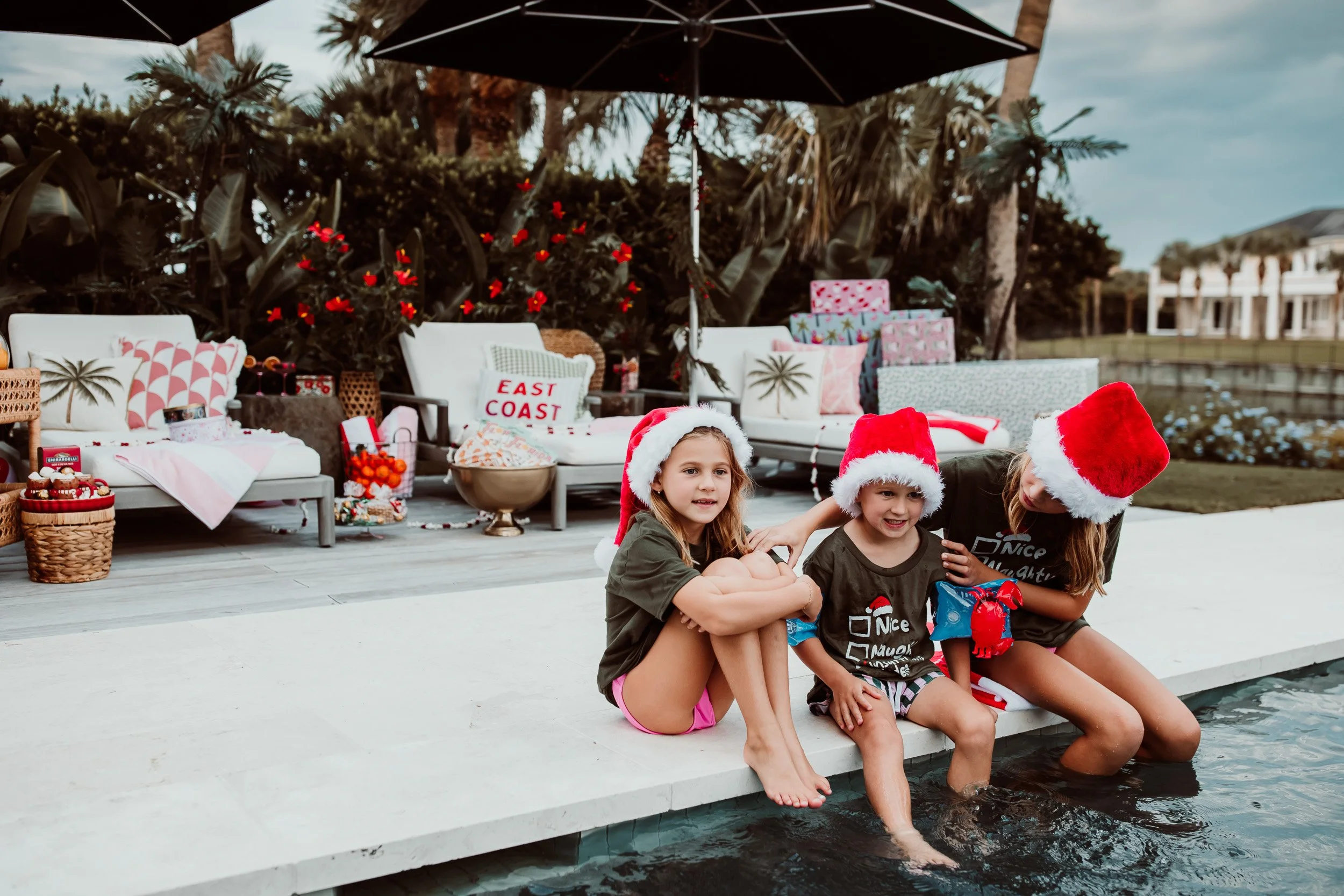 siblings sitting poolside in Santa hats and Christmas t shirts embracing during holiday family photos