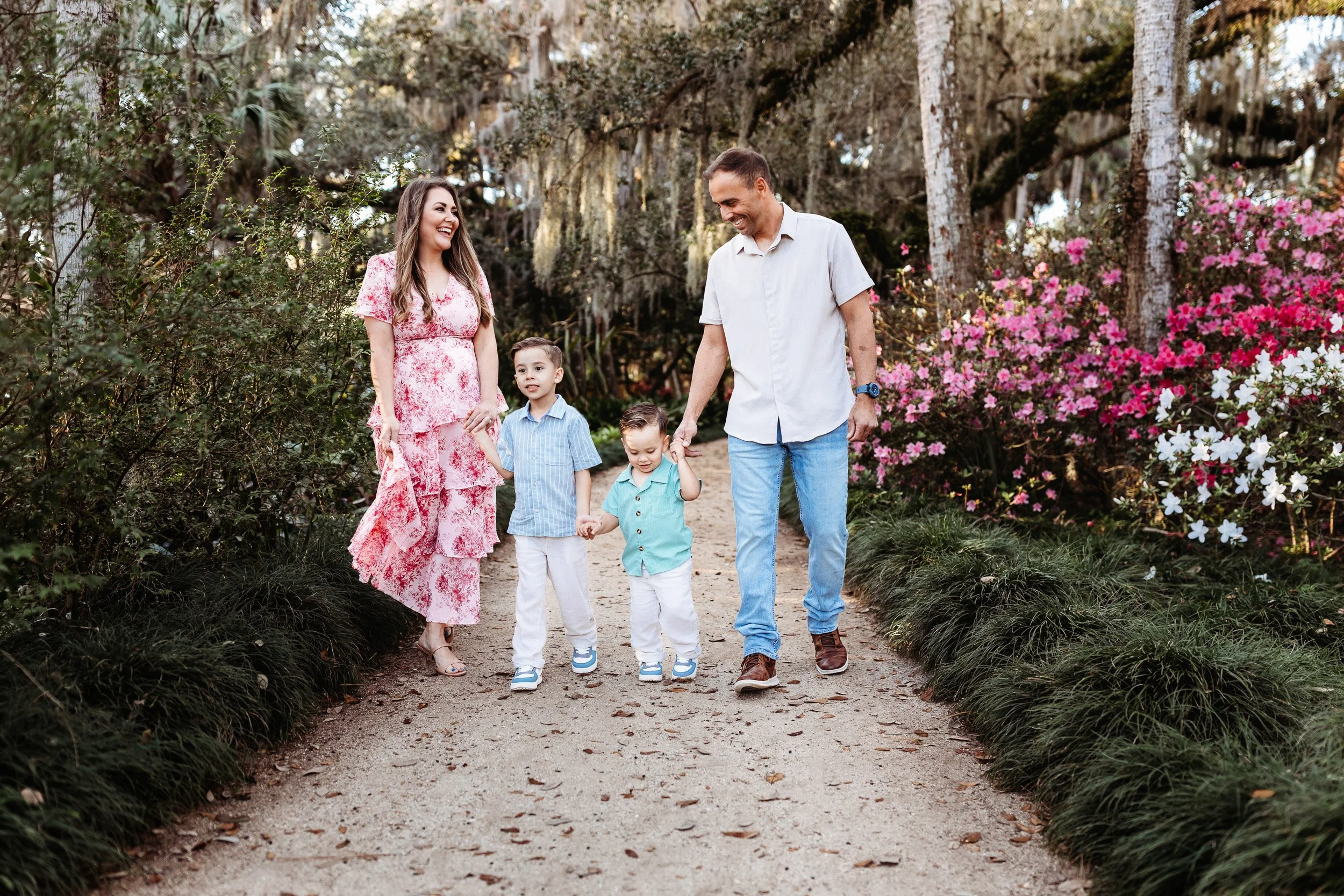 family walking on a trail hand in hand on a sandy path with azaleas in bloom around them and they are laughing