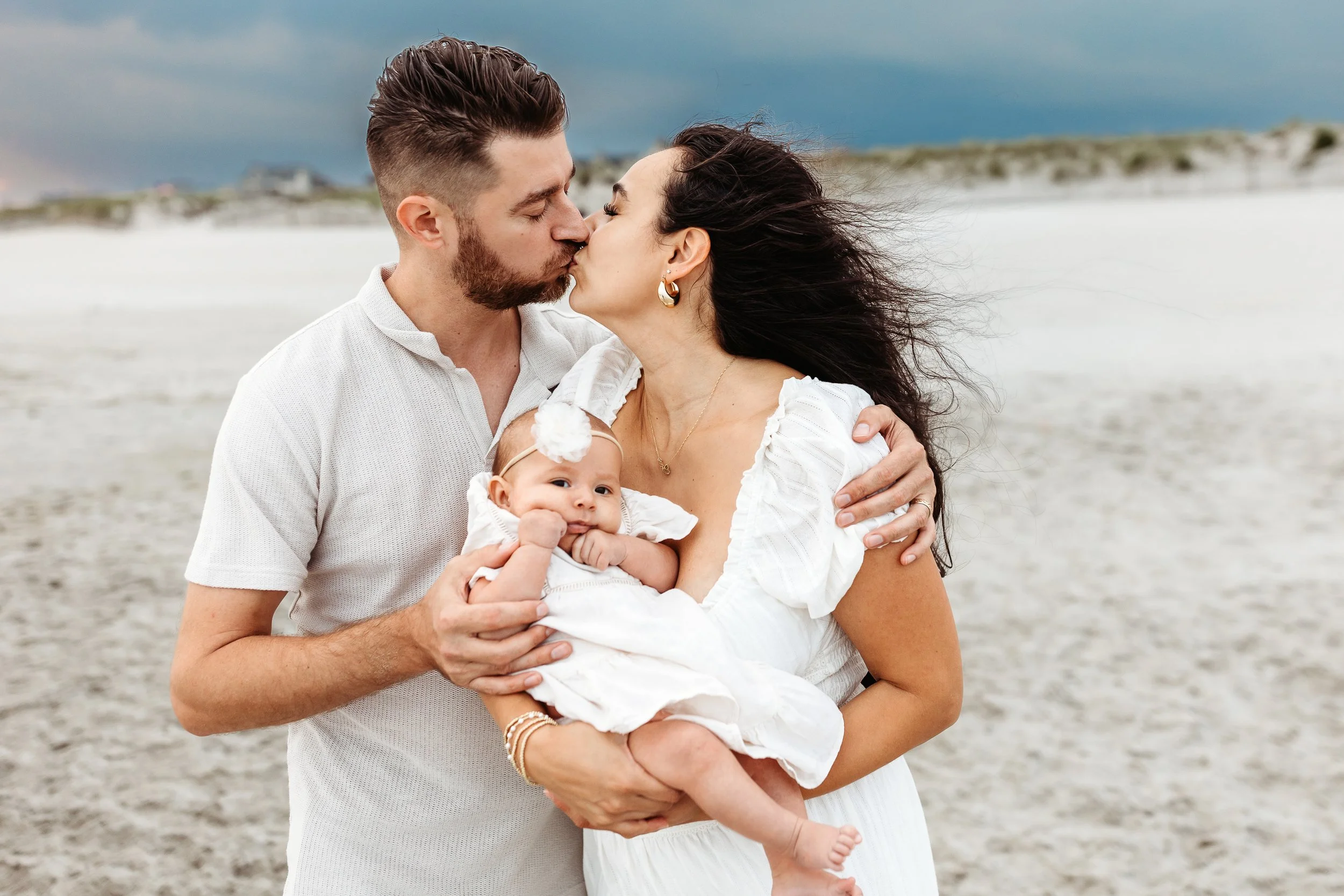 close up of husband and wife embraced and kissing while baby looks at the camera