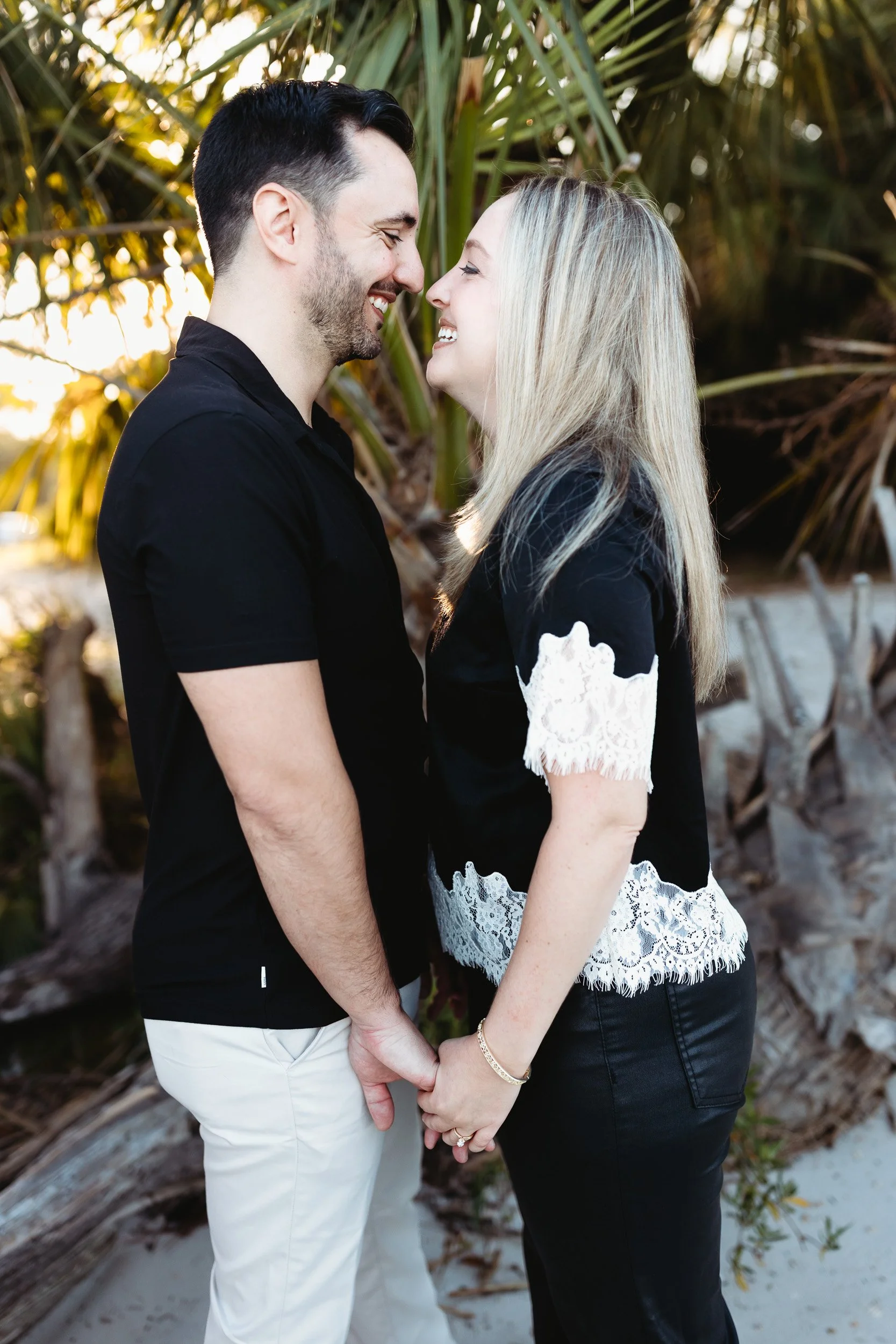 couple looking at each other holding hands in front of palm trees at sunset and they are smiling