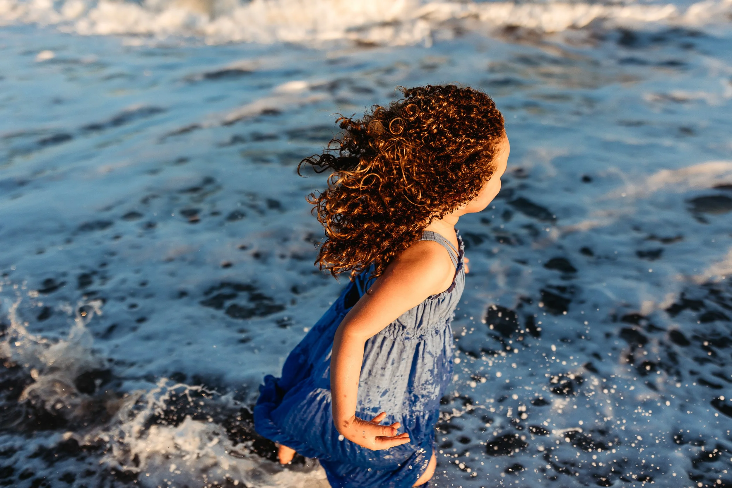 little girl running through the ocean at sunset and water is splashing all over her and the light is golden