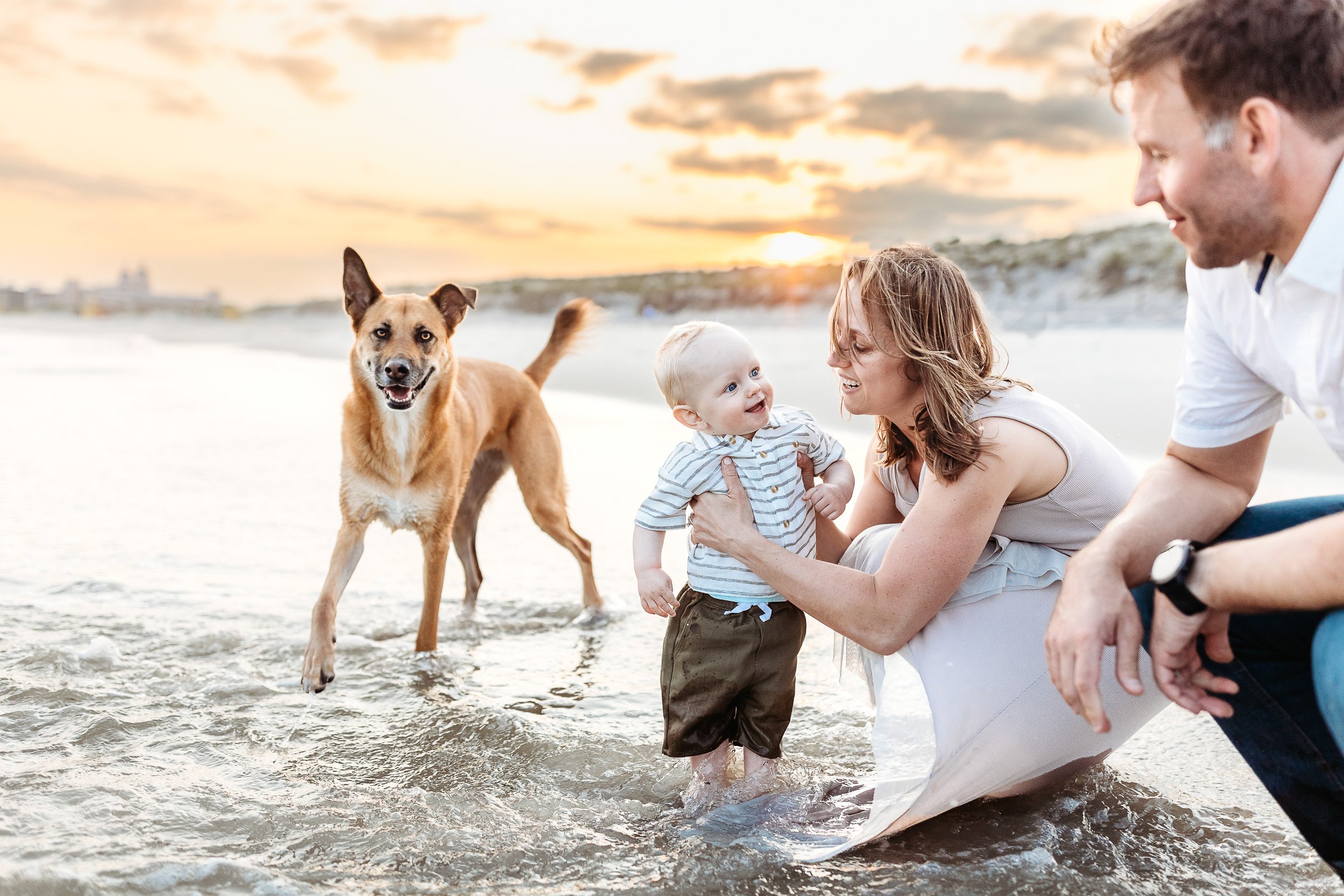 family in the water at Jacksonville beach and mom is holding a baby while a dog runs in circles around them 