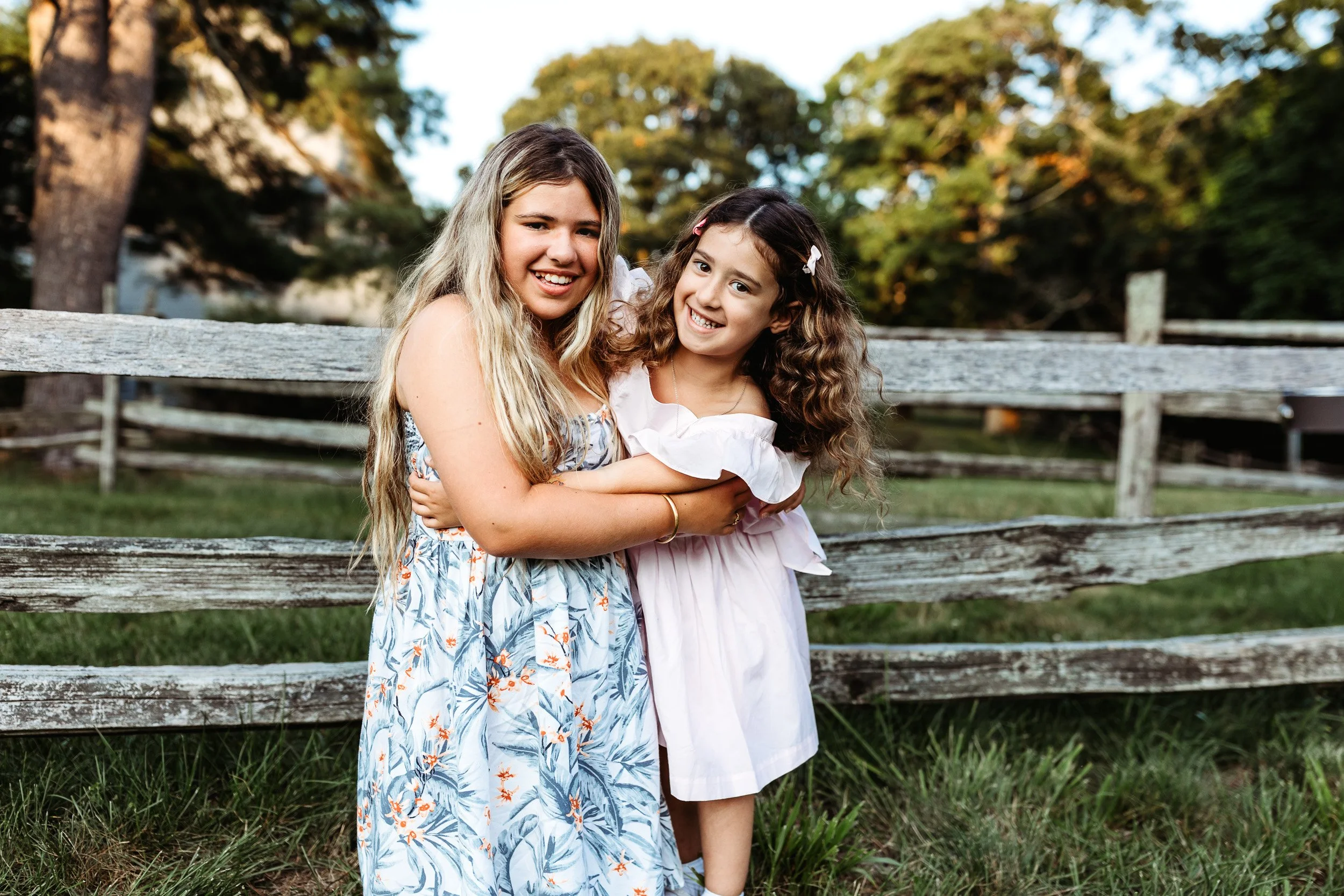 siblings embraced and laughing in front of a wooden fence