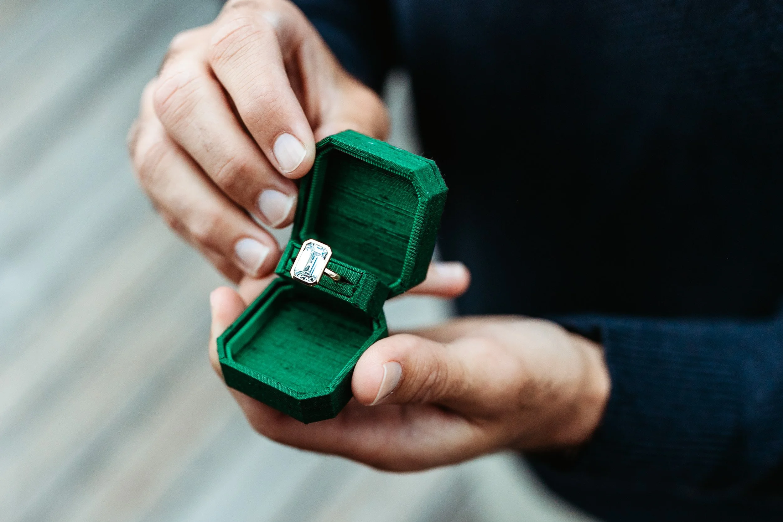 man holding green velvet ring box with very large emerald cut diamond ring in it
