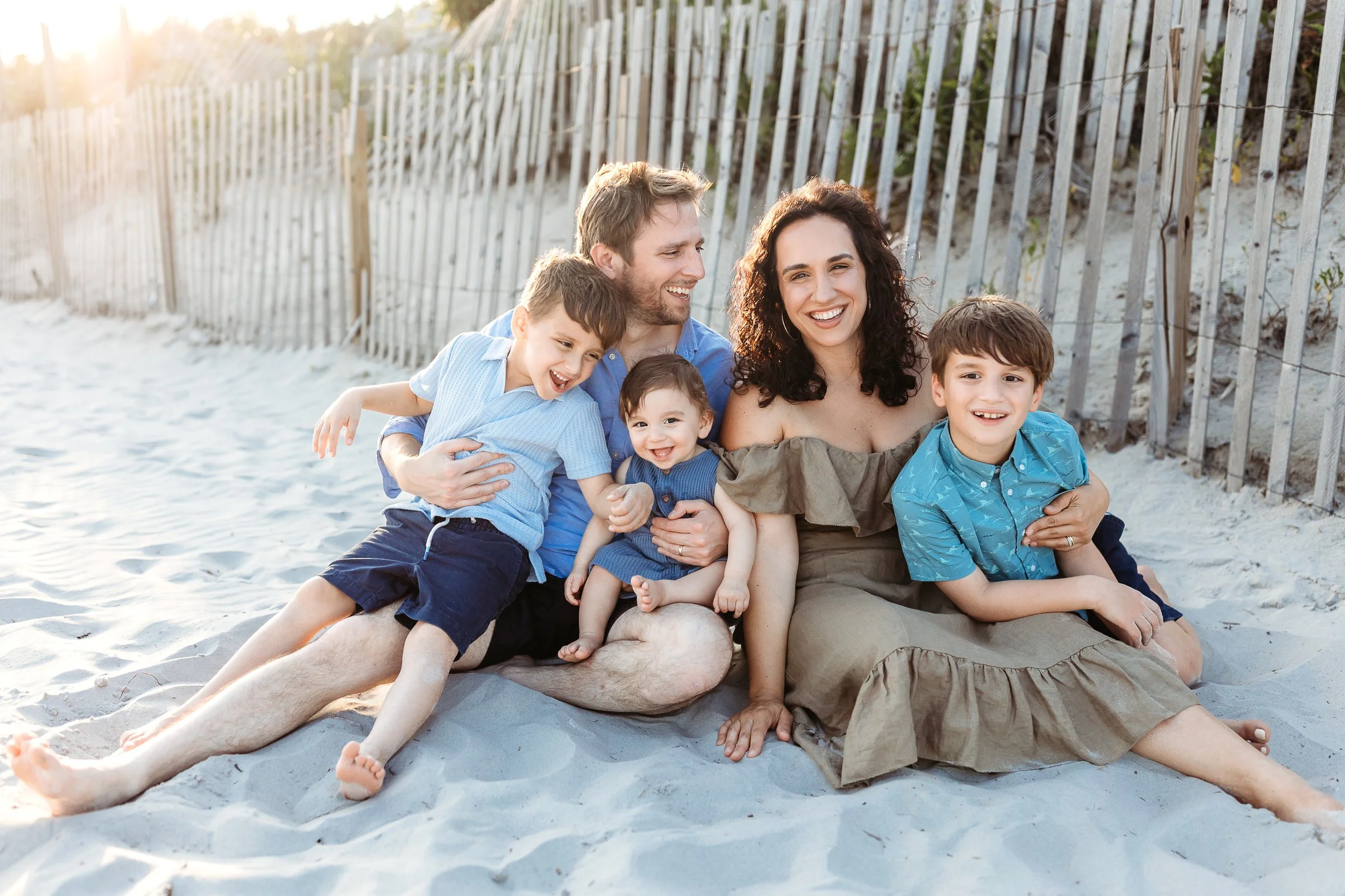 family seated on a dune and they are tickling and laughing each other