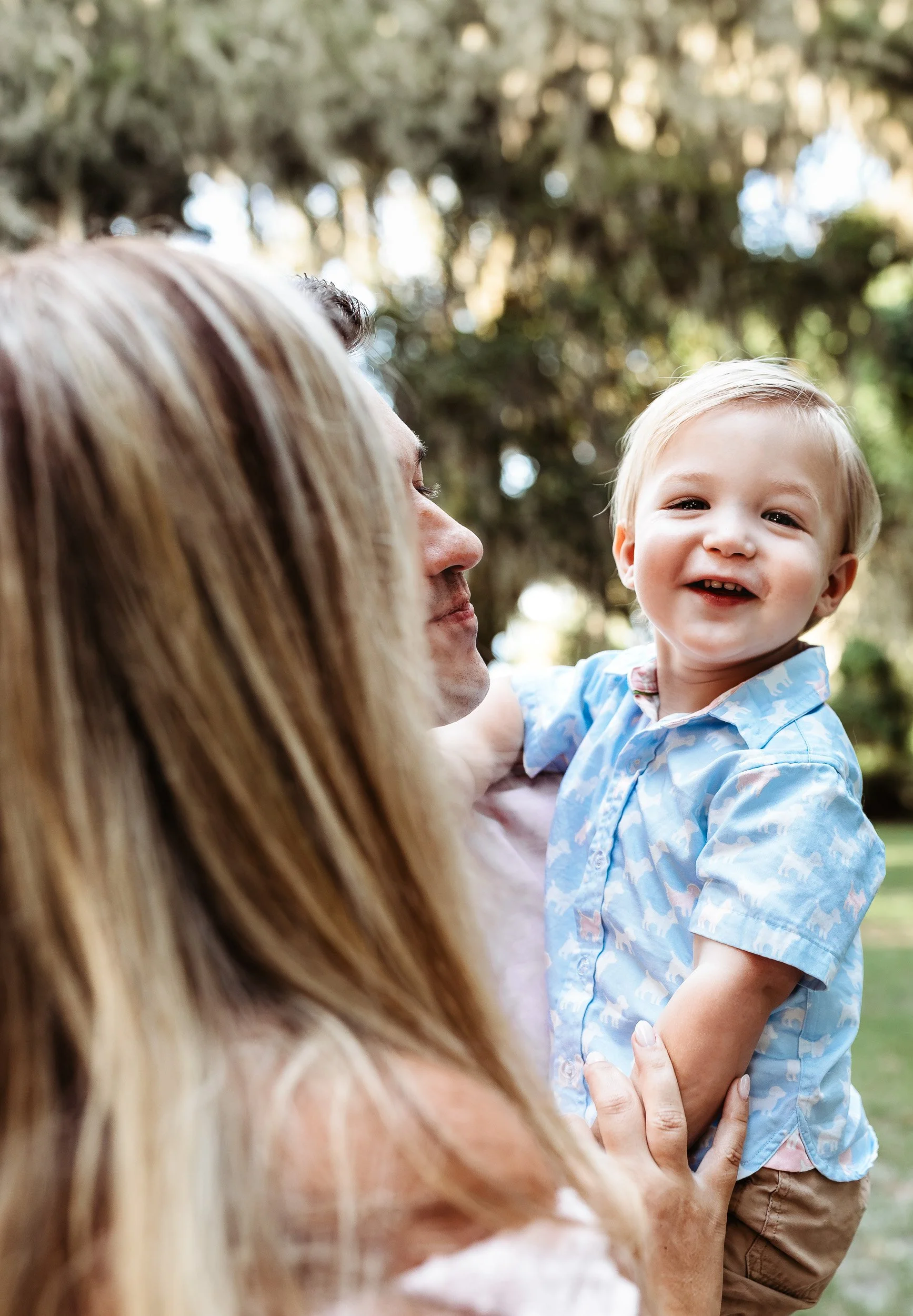 toddler laughing while looking at the camera in Jacksonville florida during maternity photos and mom is holding him while he plays peek-a-boo