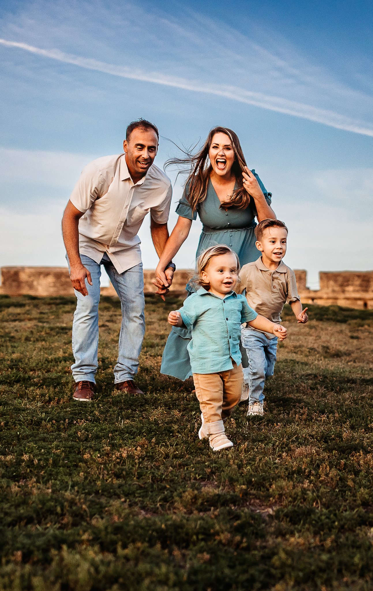 family running down a grassy hill laughing with the fort behind them