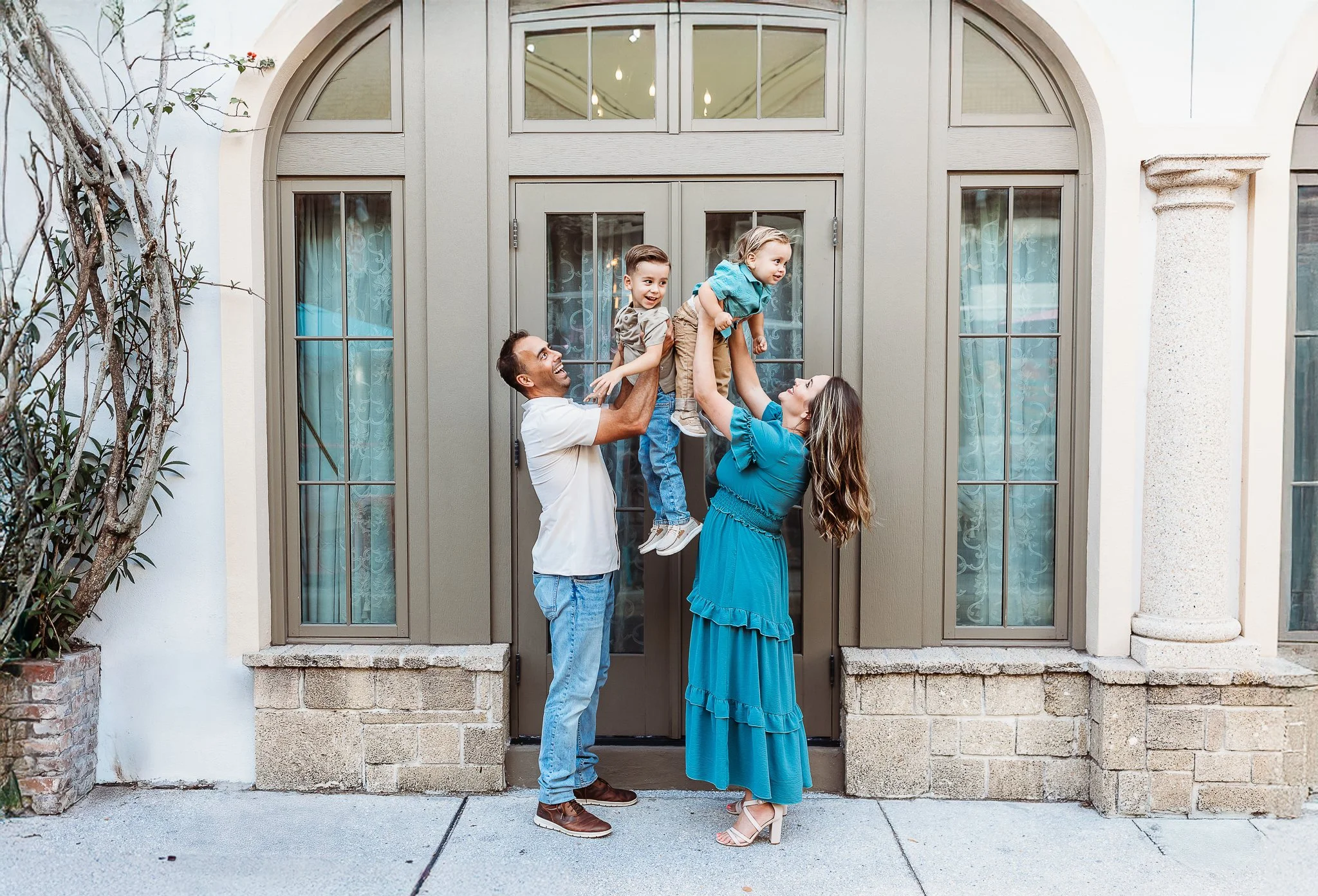 family playing with their children for family photos on the streets of st augustine in front of a tan arched glass door