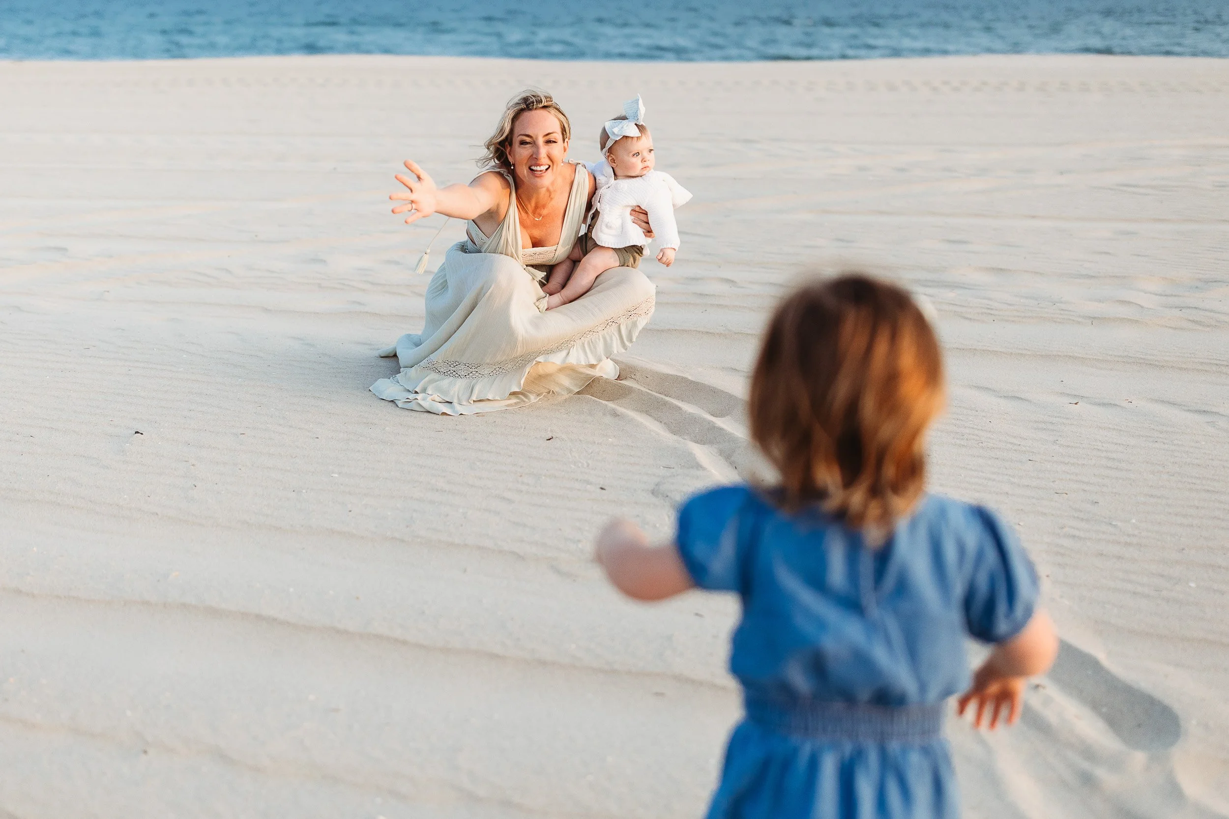 mother kneeling in the sand and her toddler daughter is running towards her during a Jacksonville family photo session