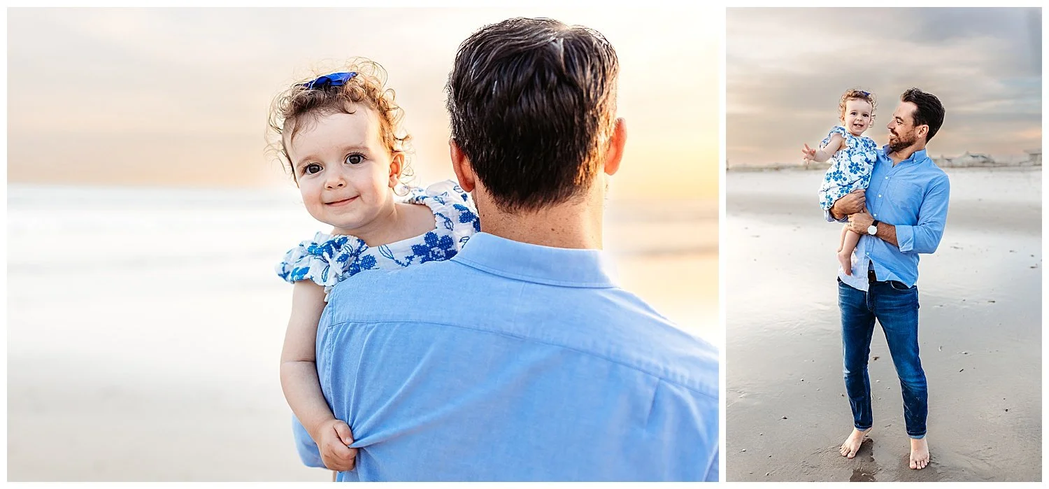 dad holding baby girl who is peaking over dad's shoulder and laughing sunset sky behind them ocean waves