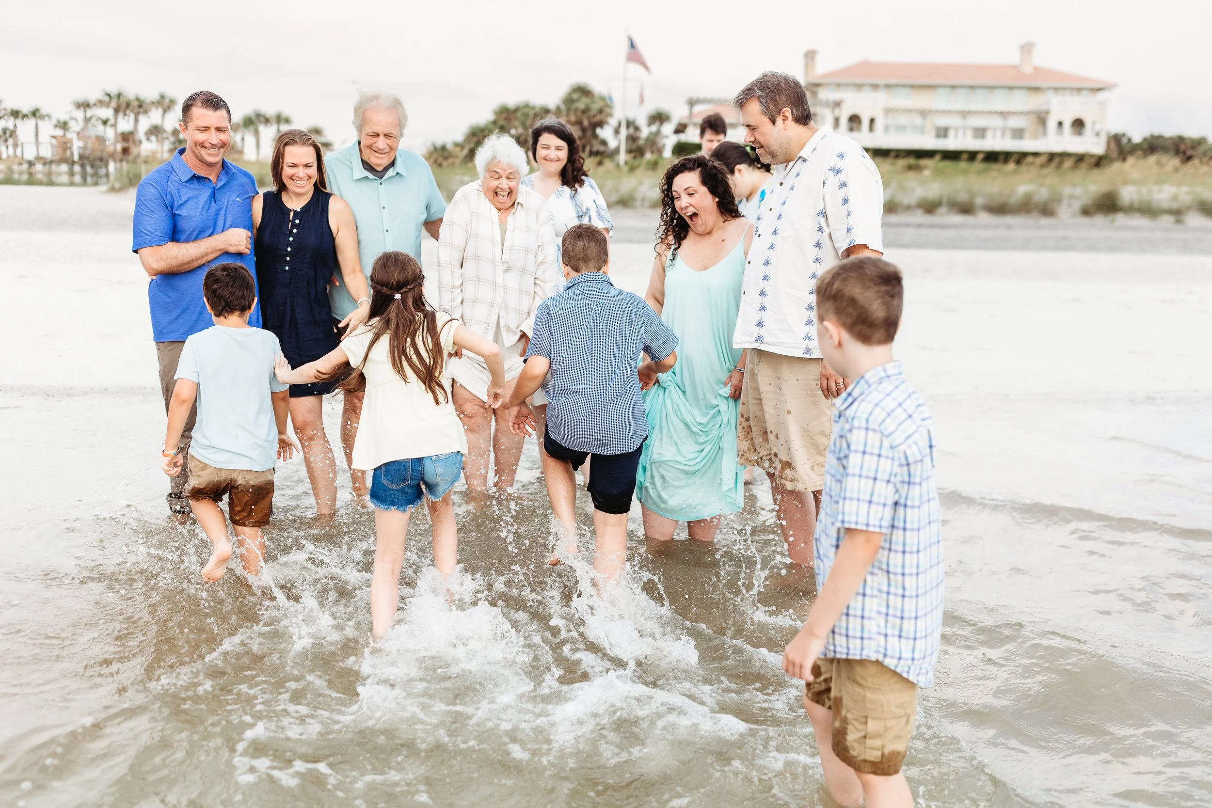 kids running towards a family and about to get them wet from the ocean and they are all laughing