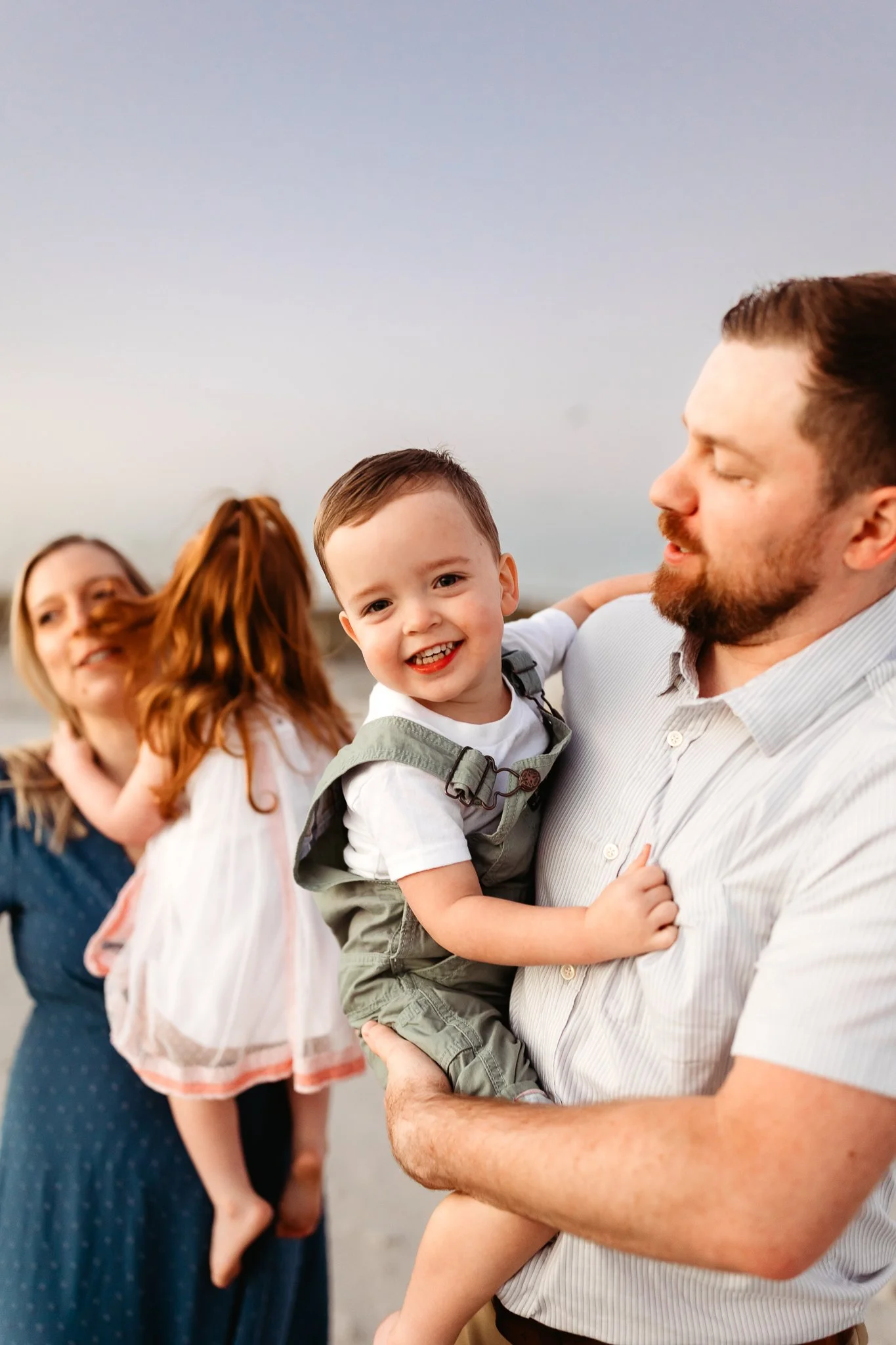 Young child laughing while being lifted into the air during a sunrise family photography session in Crescent Beach.
