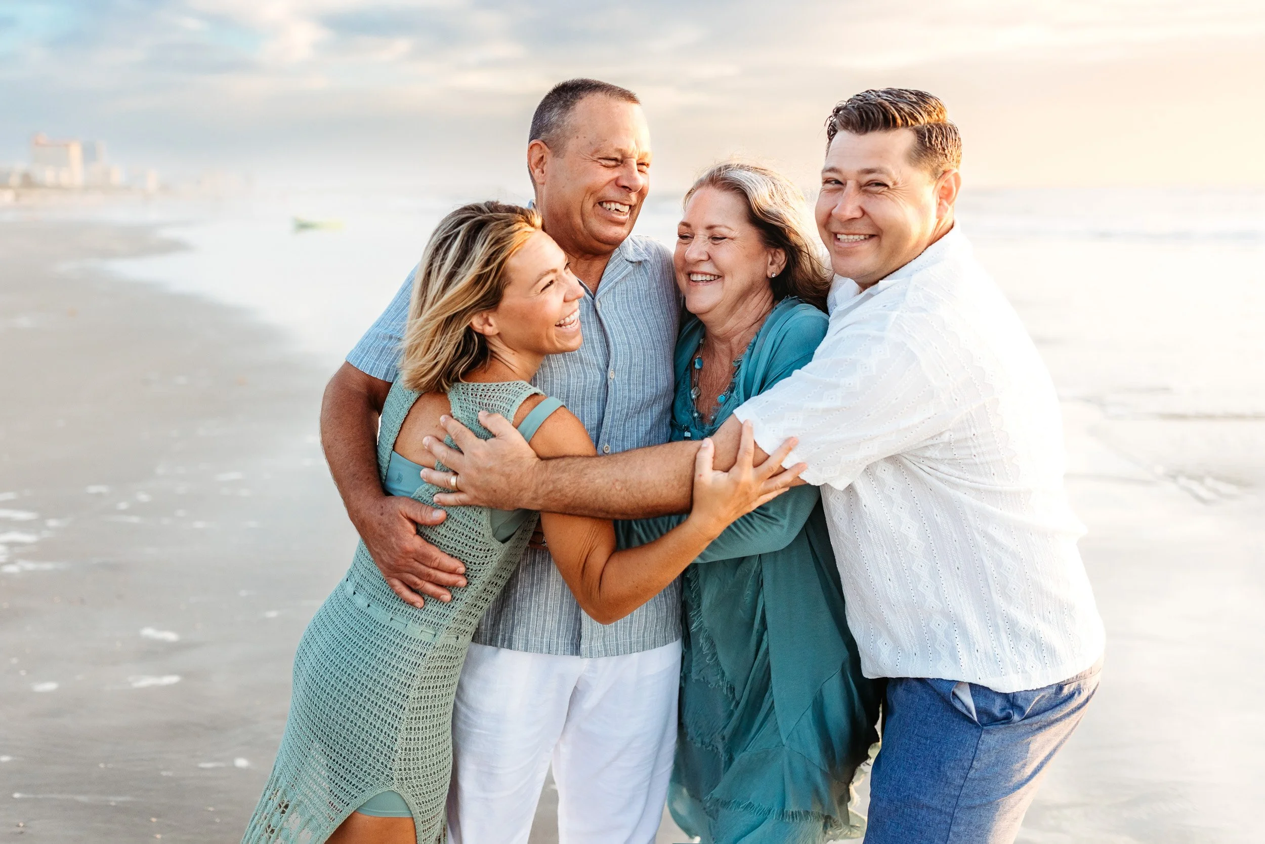 parents embracing adult children on the beach at sunrise and they are all laughing