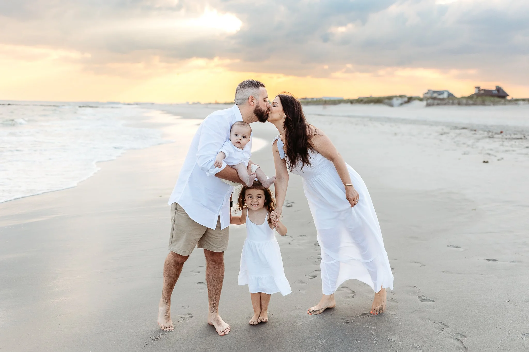 couple in white skiing while they hold a baby and toddler girl laughs and it is sunrise on st augustine beach