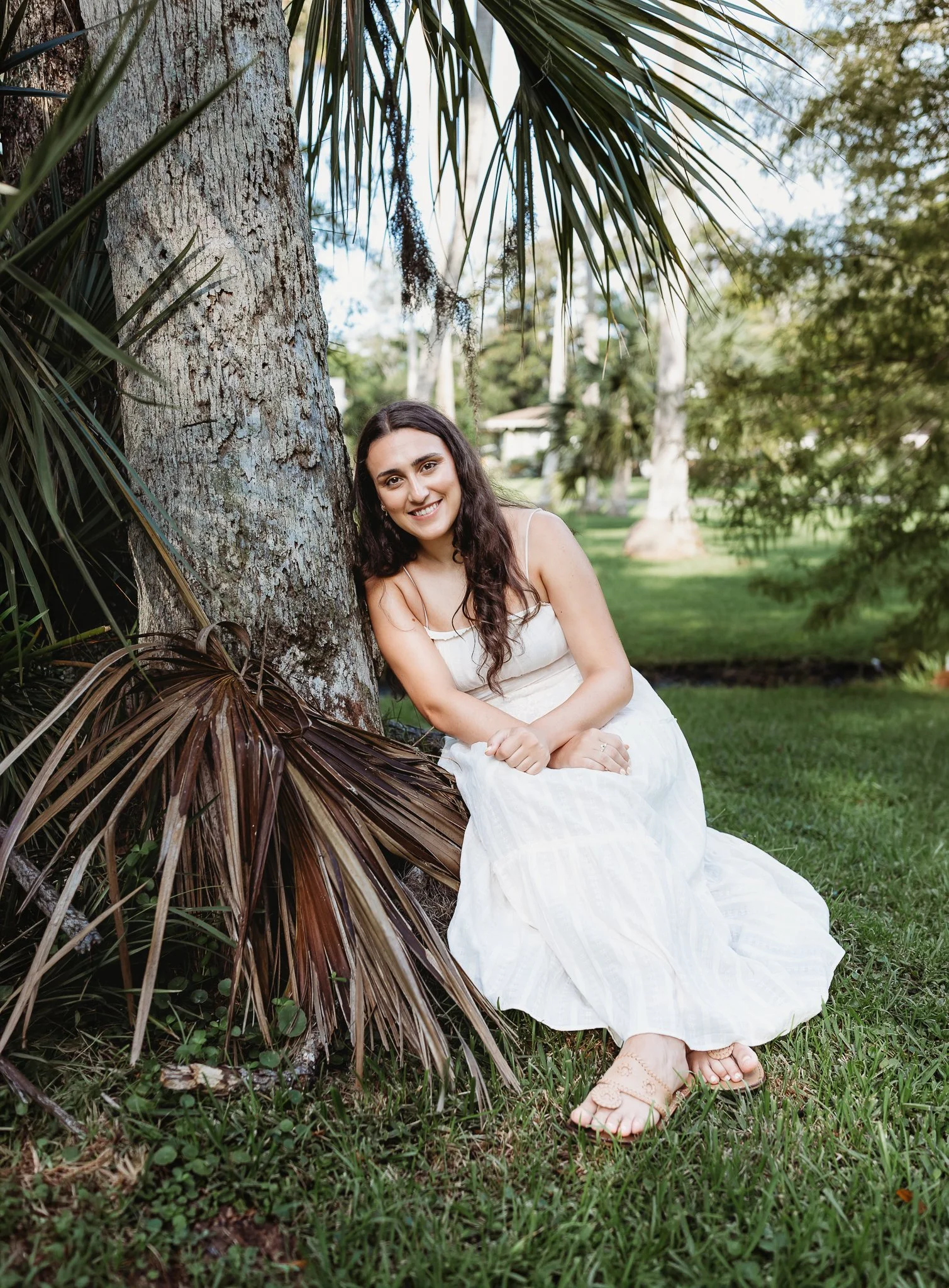 girl seated on a tree trunk with palms surrounding her for college graduation photos
