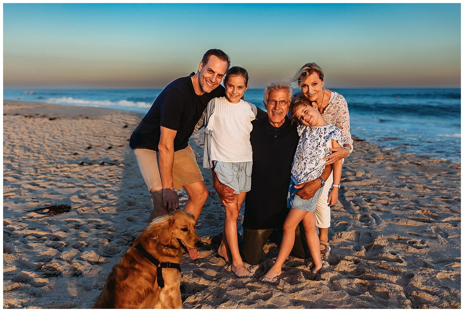 family portrait on the beach in full sun with dog and grandparents