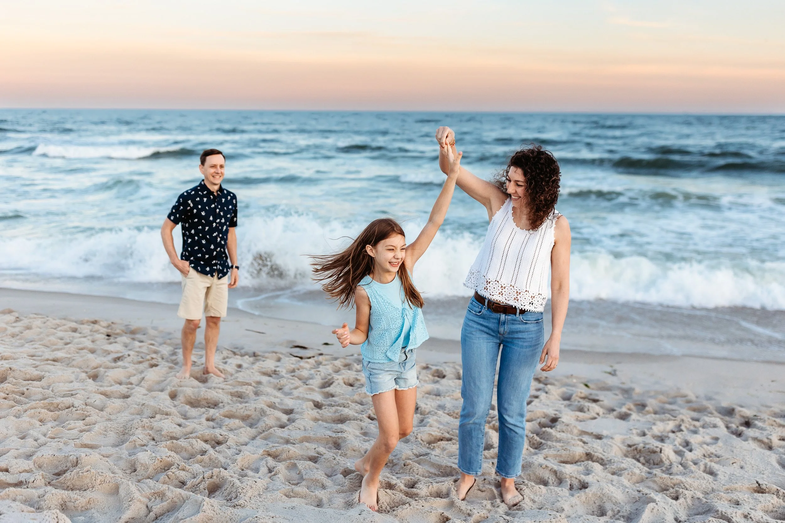 mother twirling her daughter on the beach at sunset while dad watches on the beach in villano beach