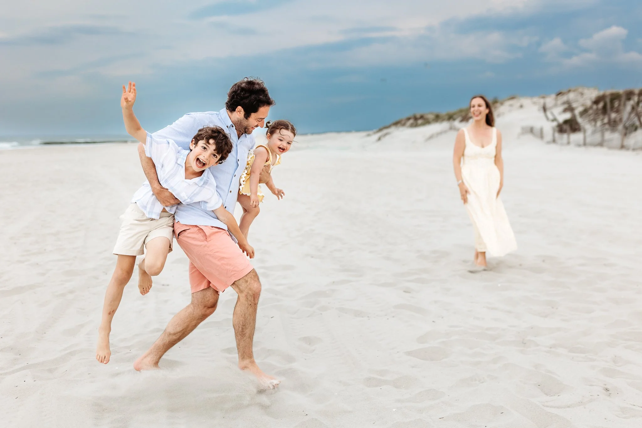dad football carrying two kids who are laughing on st augustine beach at sunset on a cloudy day and mom watches