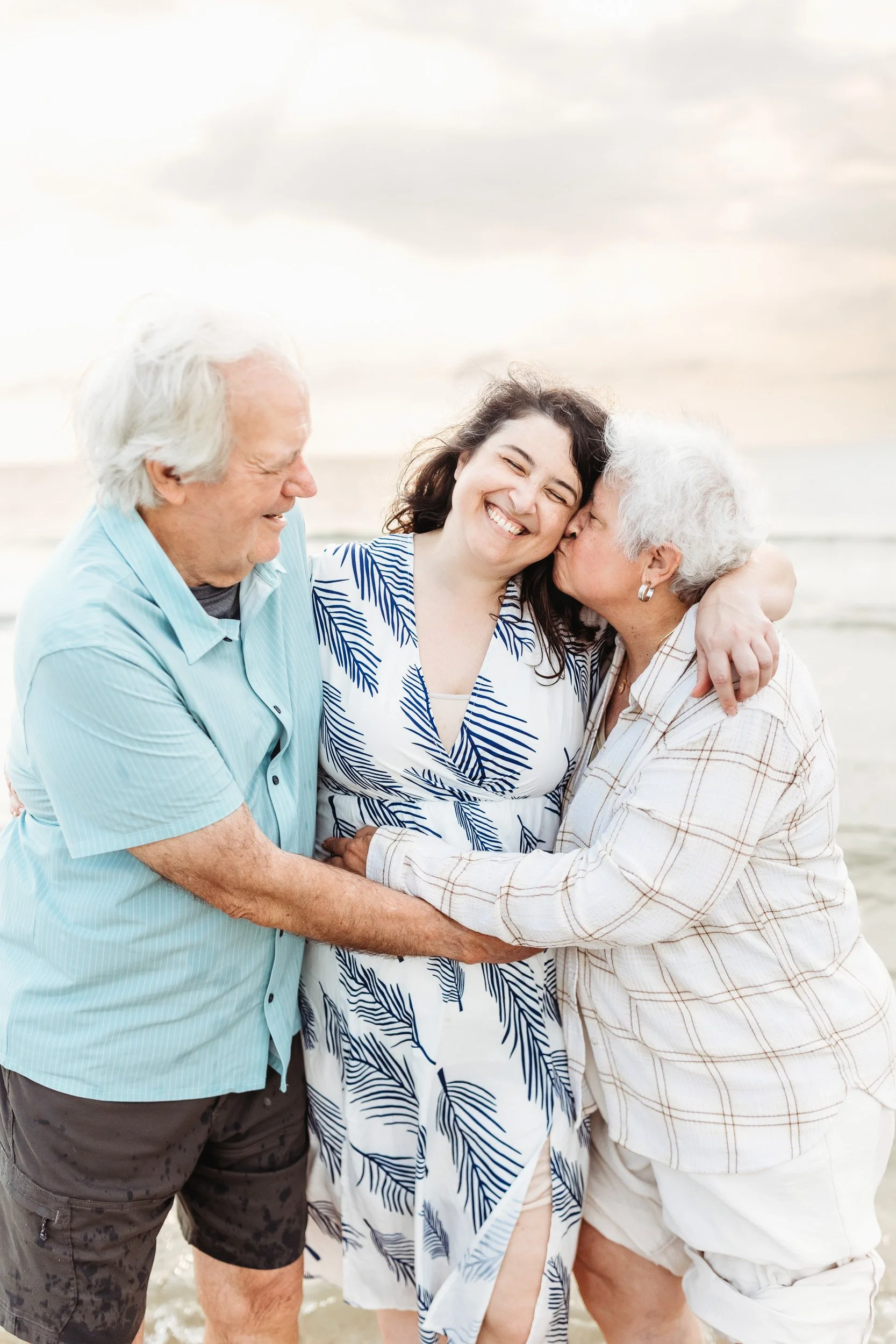 adult child being kissed by her parents on the beach at sunrise