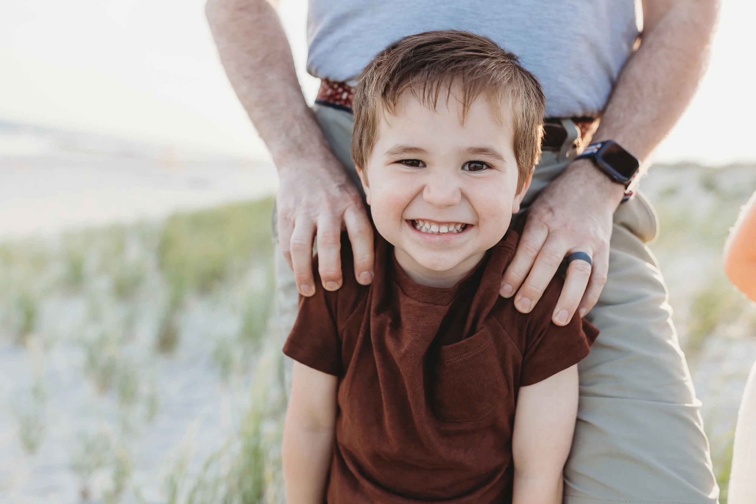 close up of boy in simple brown t shirt at Jacksonville beach at sunset and smiling for family photos