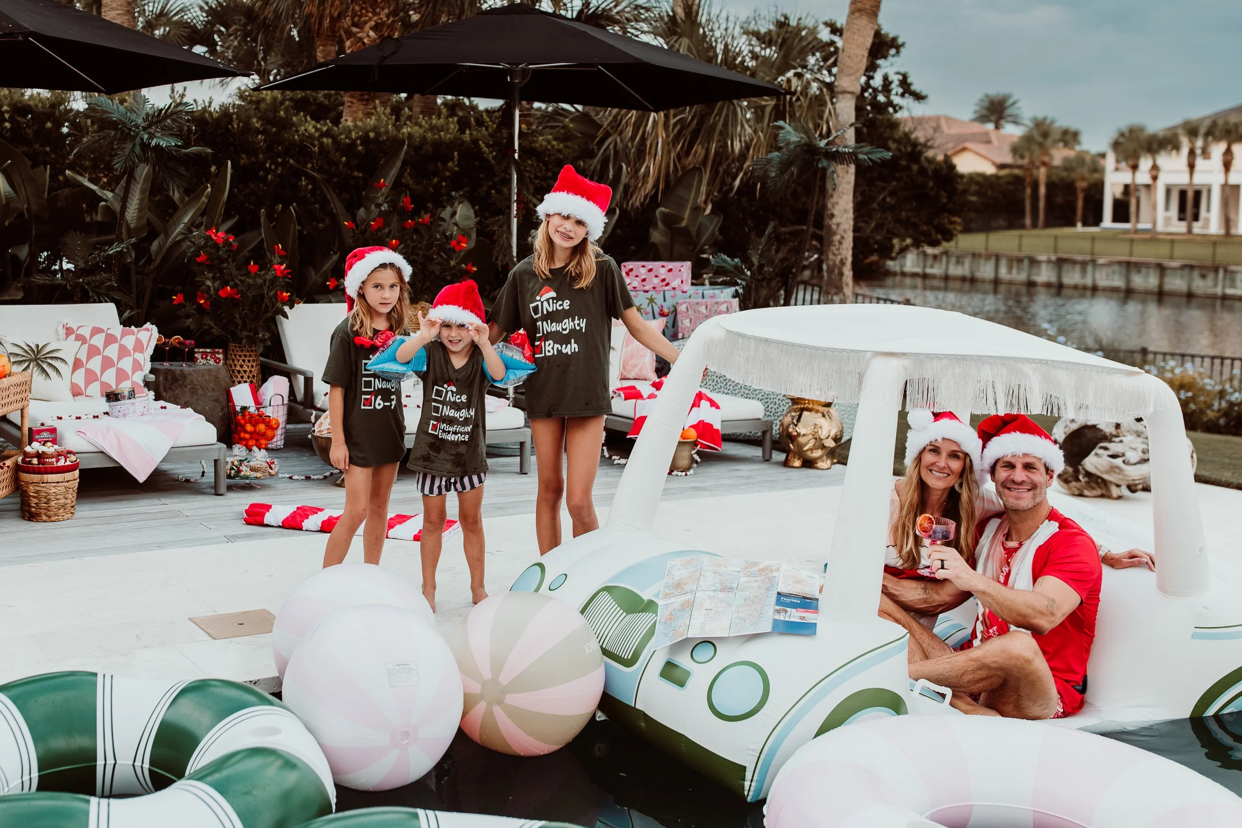 parets in an inflatable golf cart floating in a pool while their children are standing poolside in holiday t shirts and Santa hats