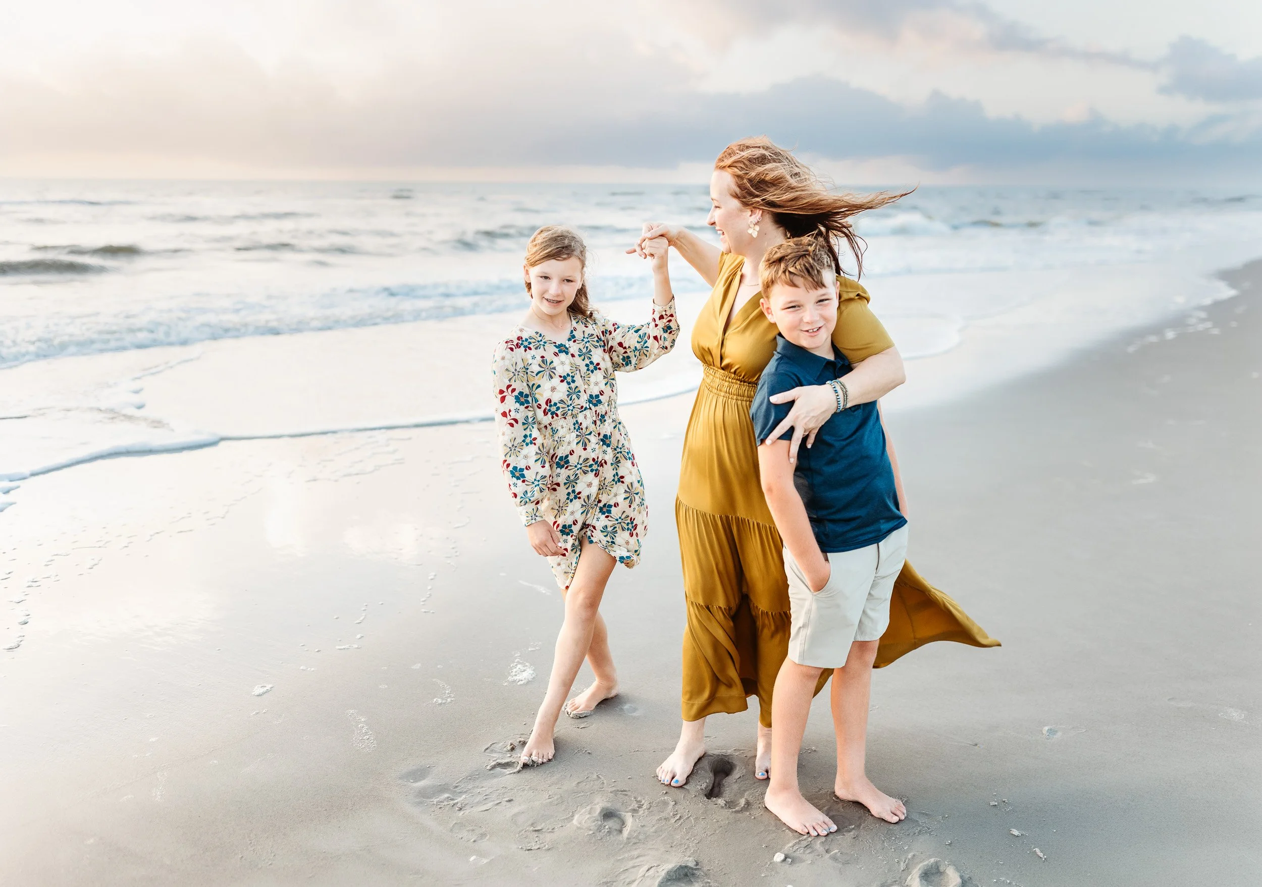 mother twirling her daughter on the beach while holding her son who is laughing