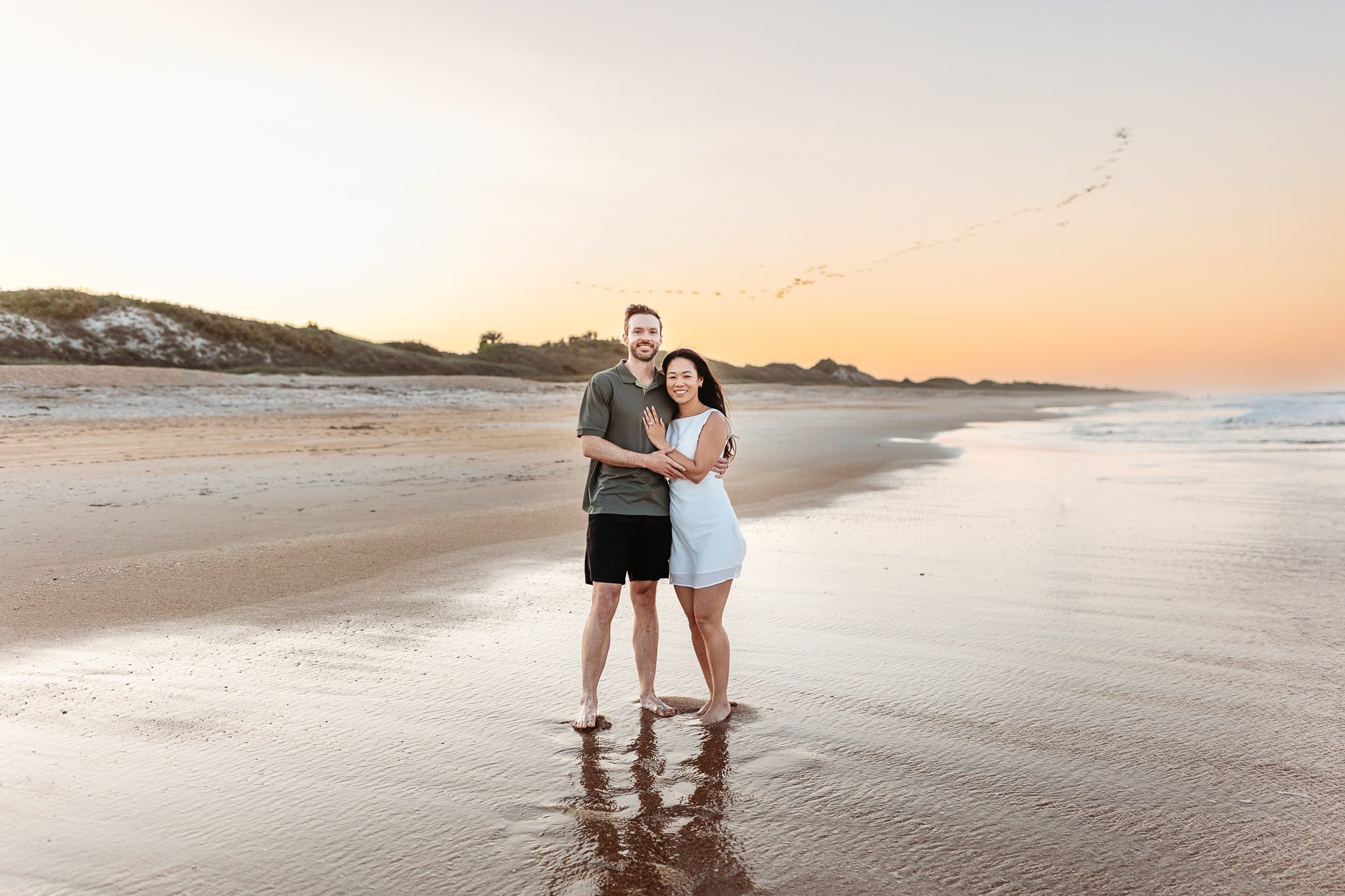 couple on the beach at sunset and a flock of birds are overhead