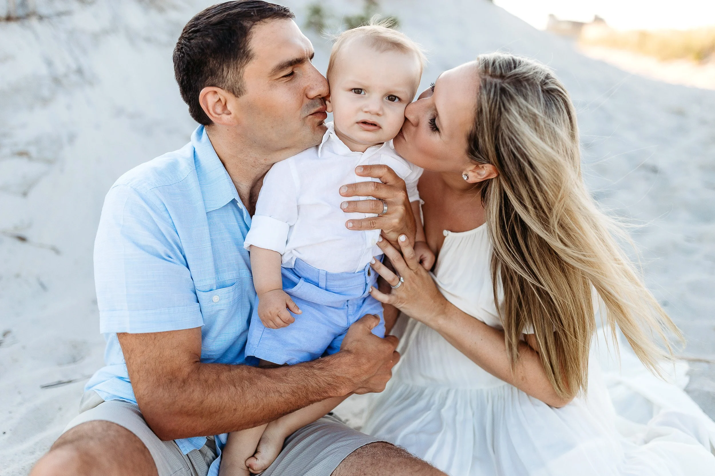 husband and wife kissing baby boy on the beach during family photo session on the beach of st augustine
