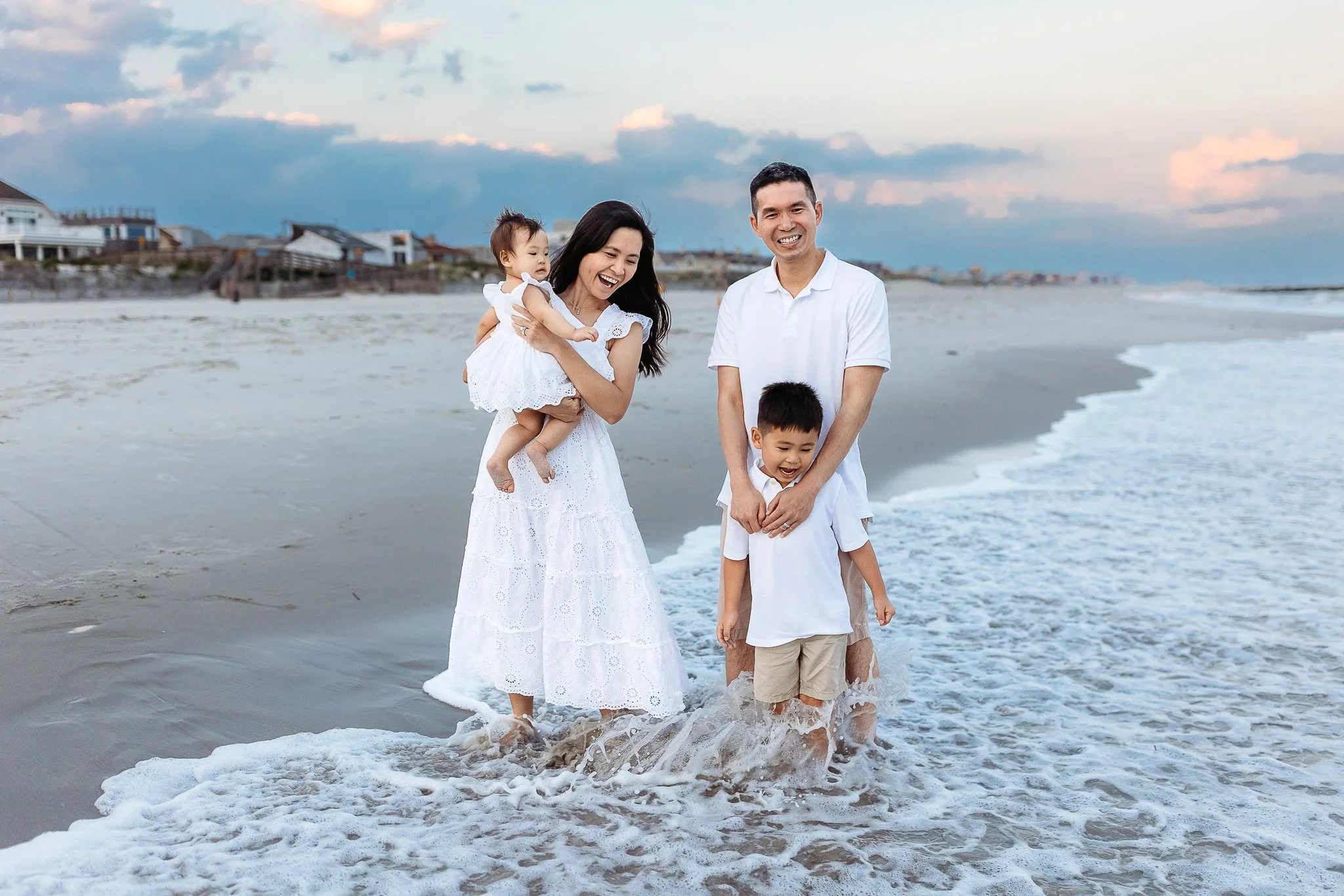 family playing in the ocean at st augustine beach dressed in white outfits and they are laughing 