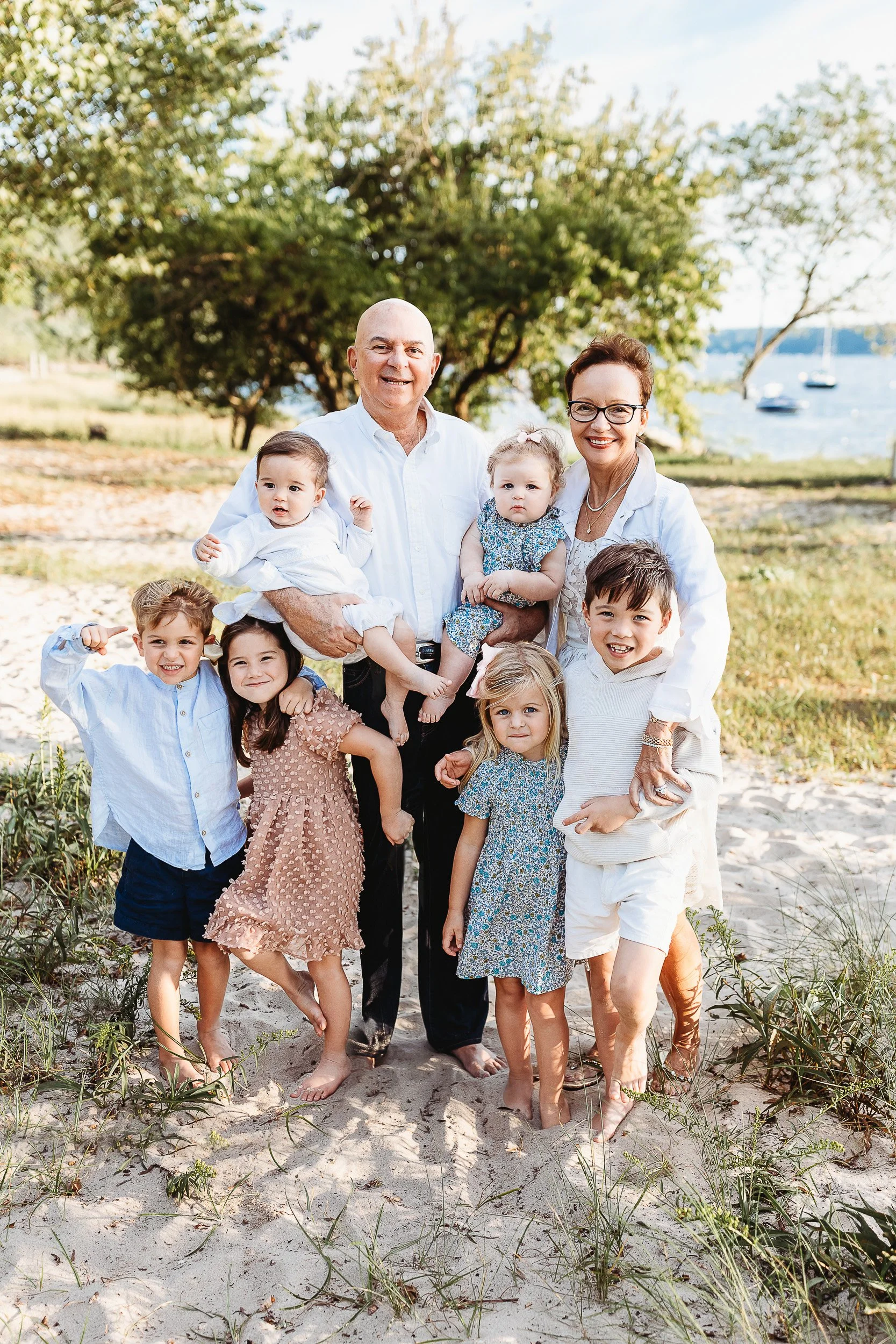 grandparents with their grandchildren and both are holding the babies while the toddlers hug them.  There are sailboats in the background and they are near the Lions Bridge in St Augustine 