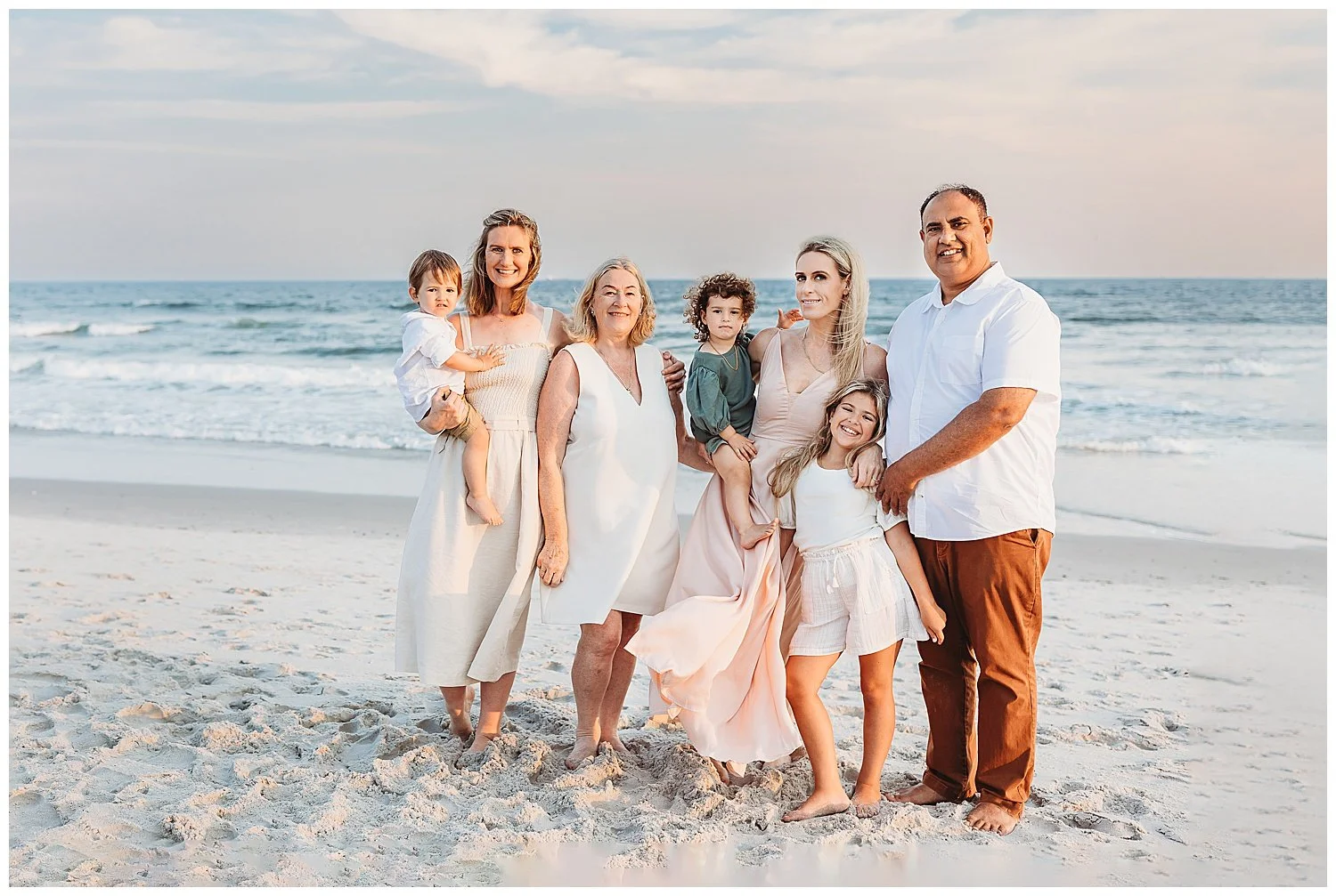 family photo of grandparents siblings and grandchildrne on the beach in front of ocean in pink tan and brown