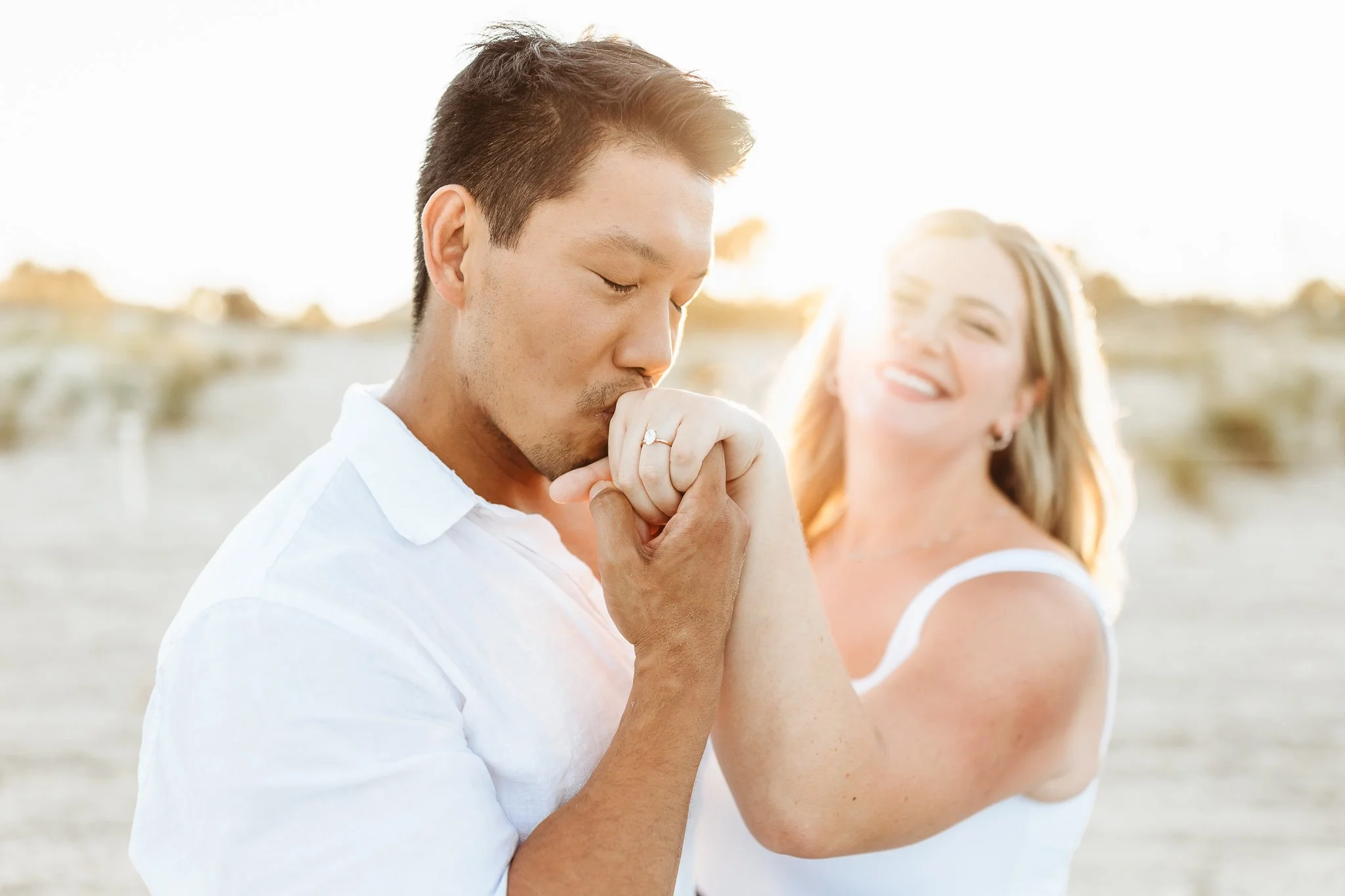 a man kissing a woman's hand at sunset with an engagement ring after proposing