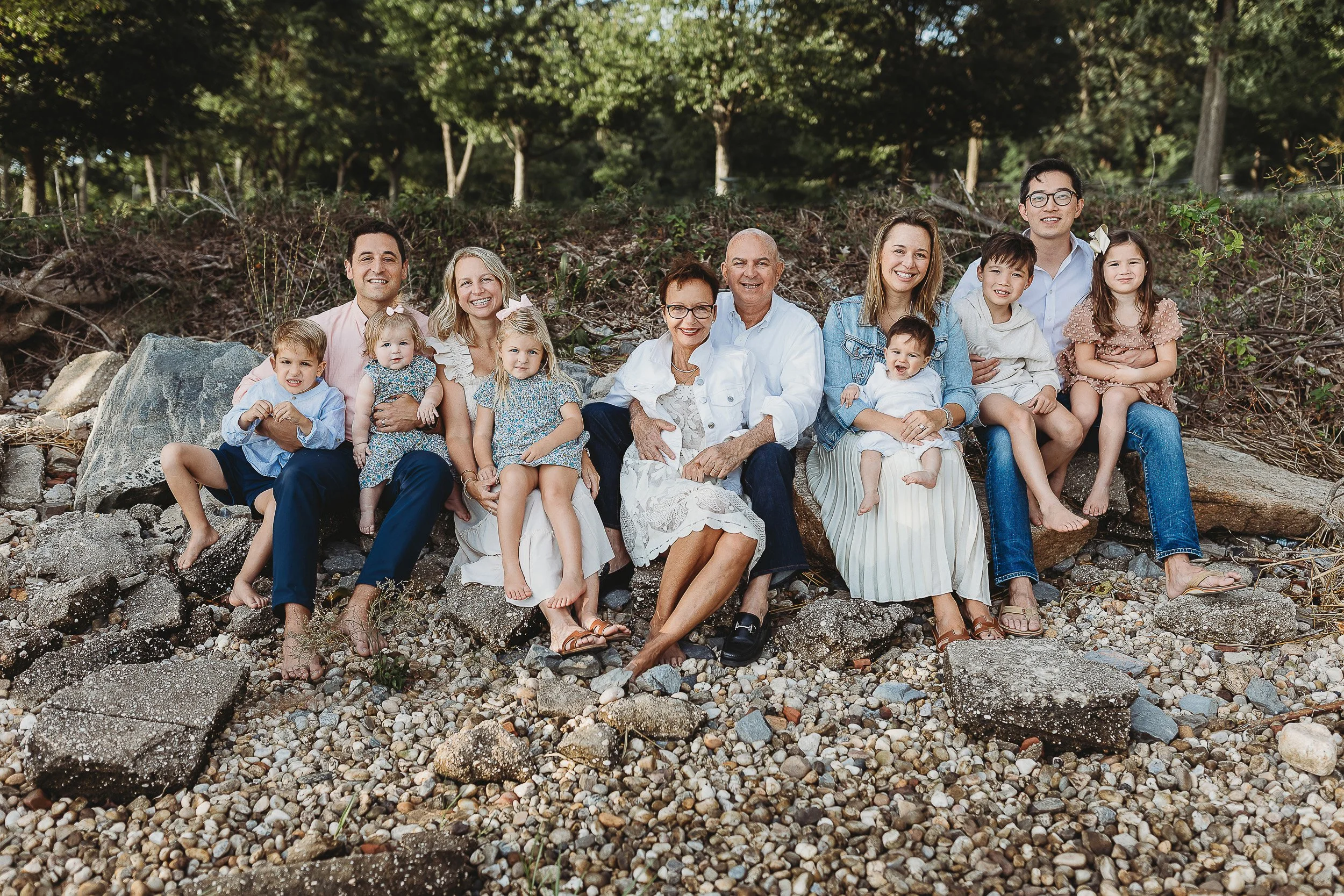 large group family seated on rocks and grandchildren on laps on a rocky shoreline 