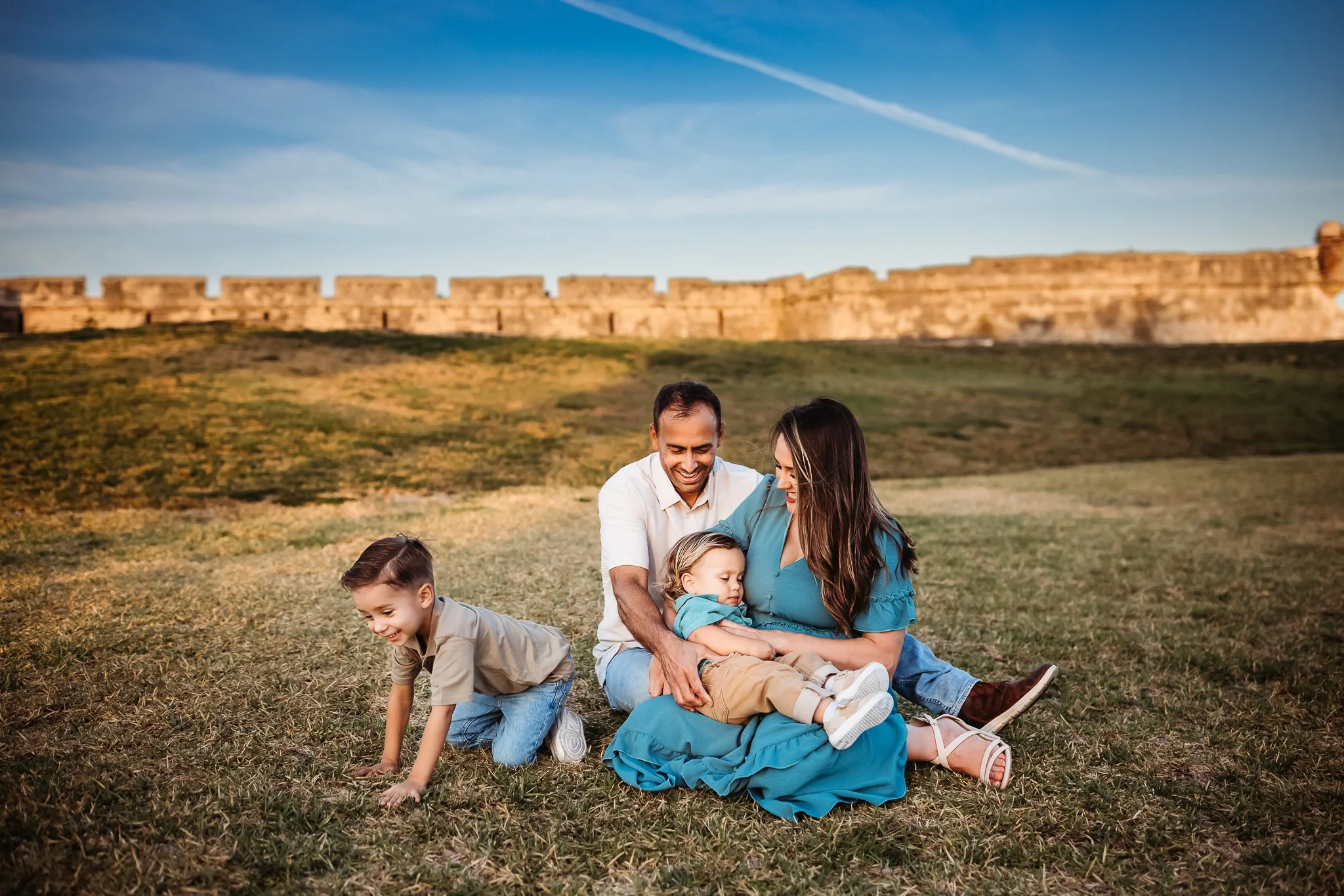 family at the fort in historic st augustine seated on the grass and playing with the fort behind them for family photos