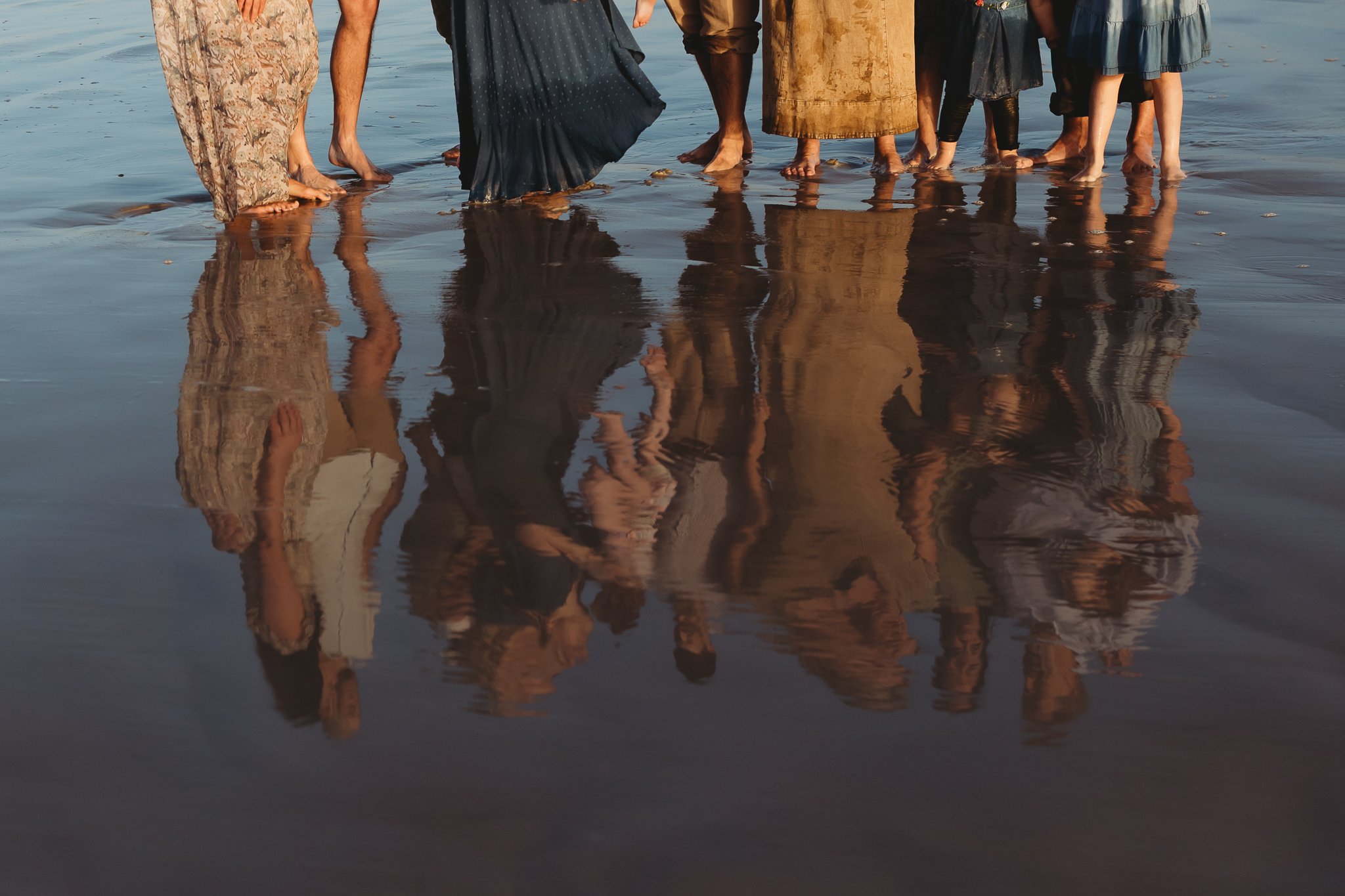 Reflection of a family’s feet and clothing in shallow ocean water during a sunrise beach photo session.