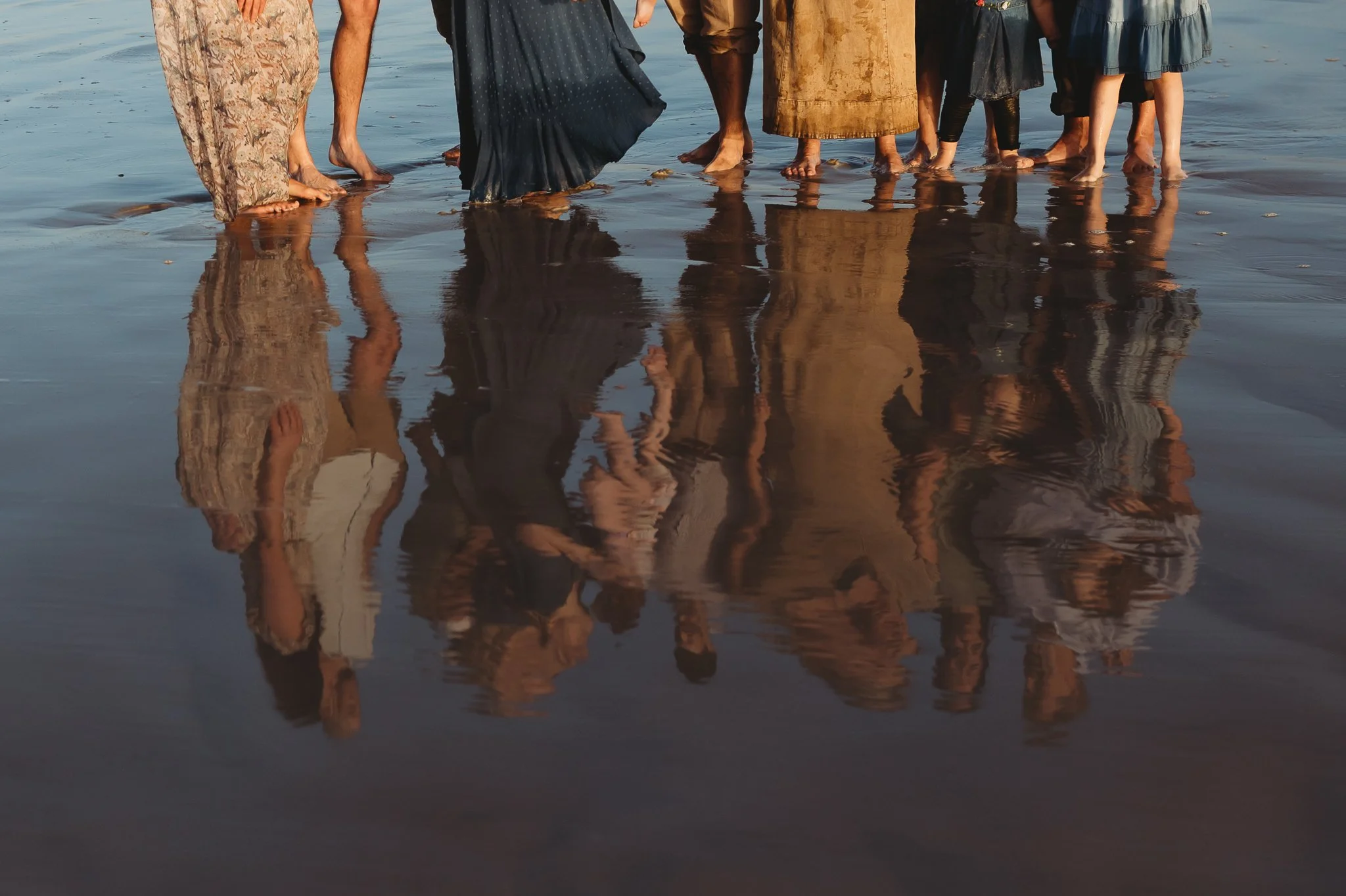 Reflection of a family’s feet and clothing in shallow ocean water during a sunrise beach photo session.