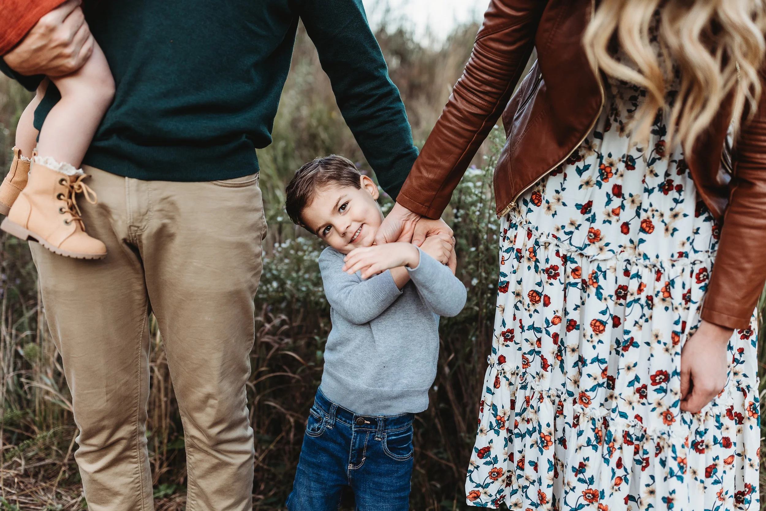 close up of boy hugging mom's arm in front of wildflowers