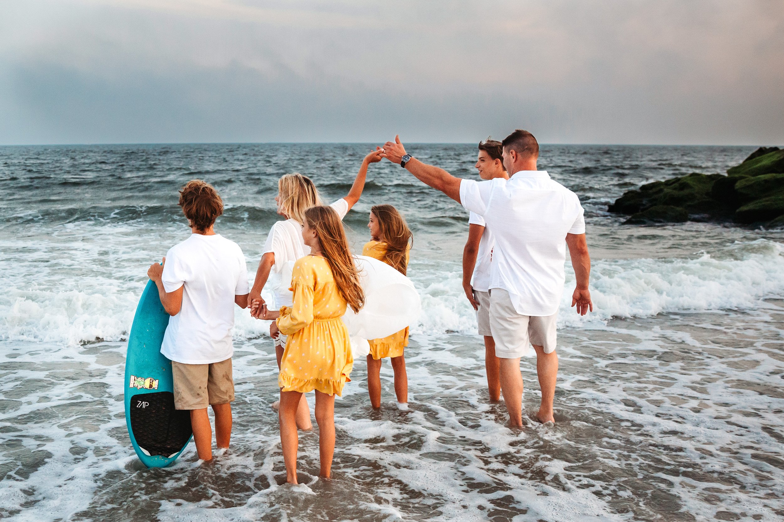 mother and father holding hands in the ocean while the children play during family photos in Jacksonville
