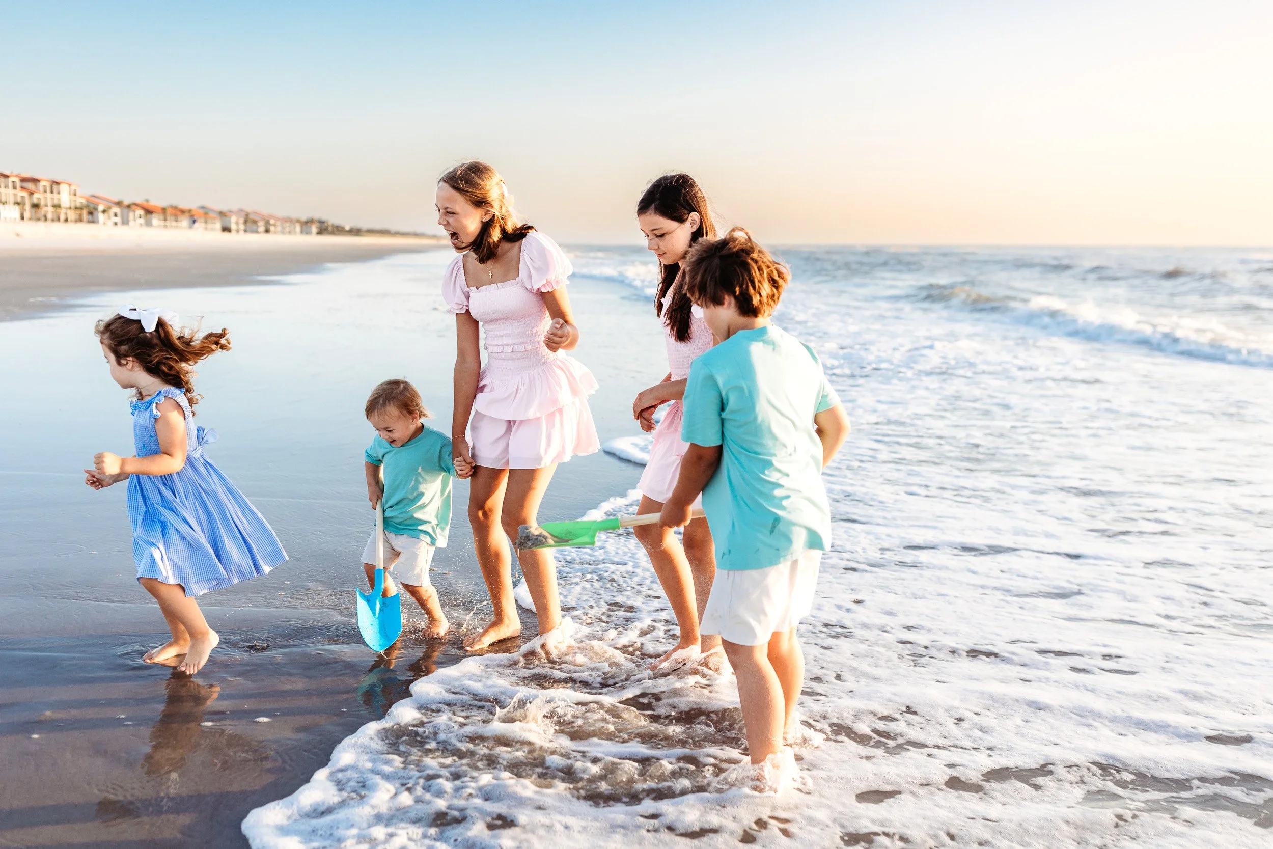 cousins playing in the ocean and one little boy has a shovel and they are laughing