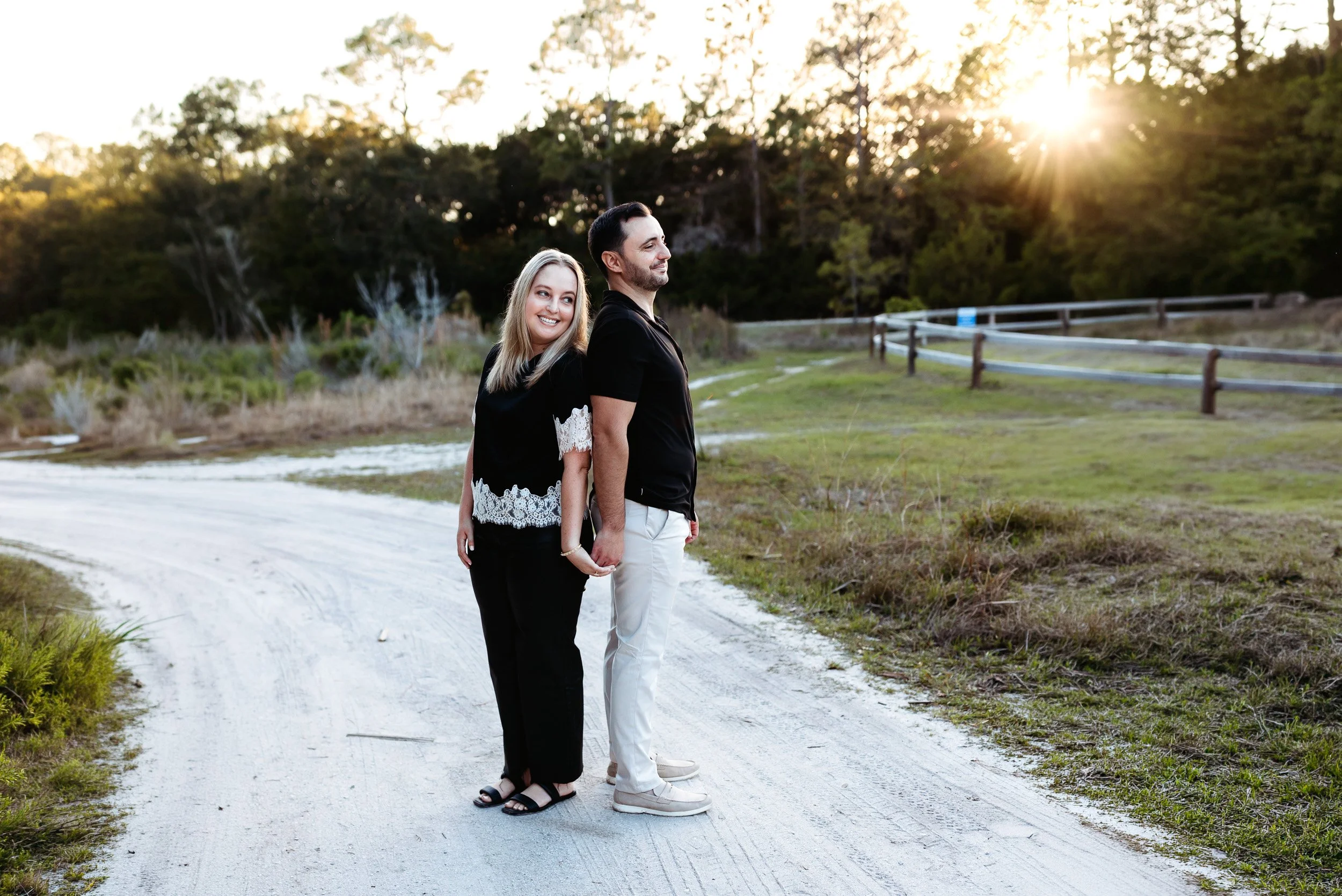 couple leaning back to back during sunset after getting engaged on the water