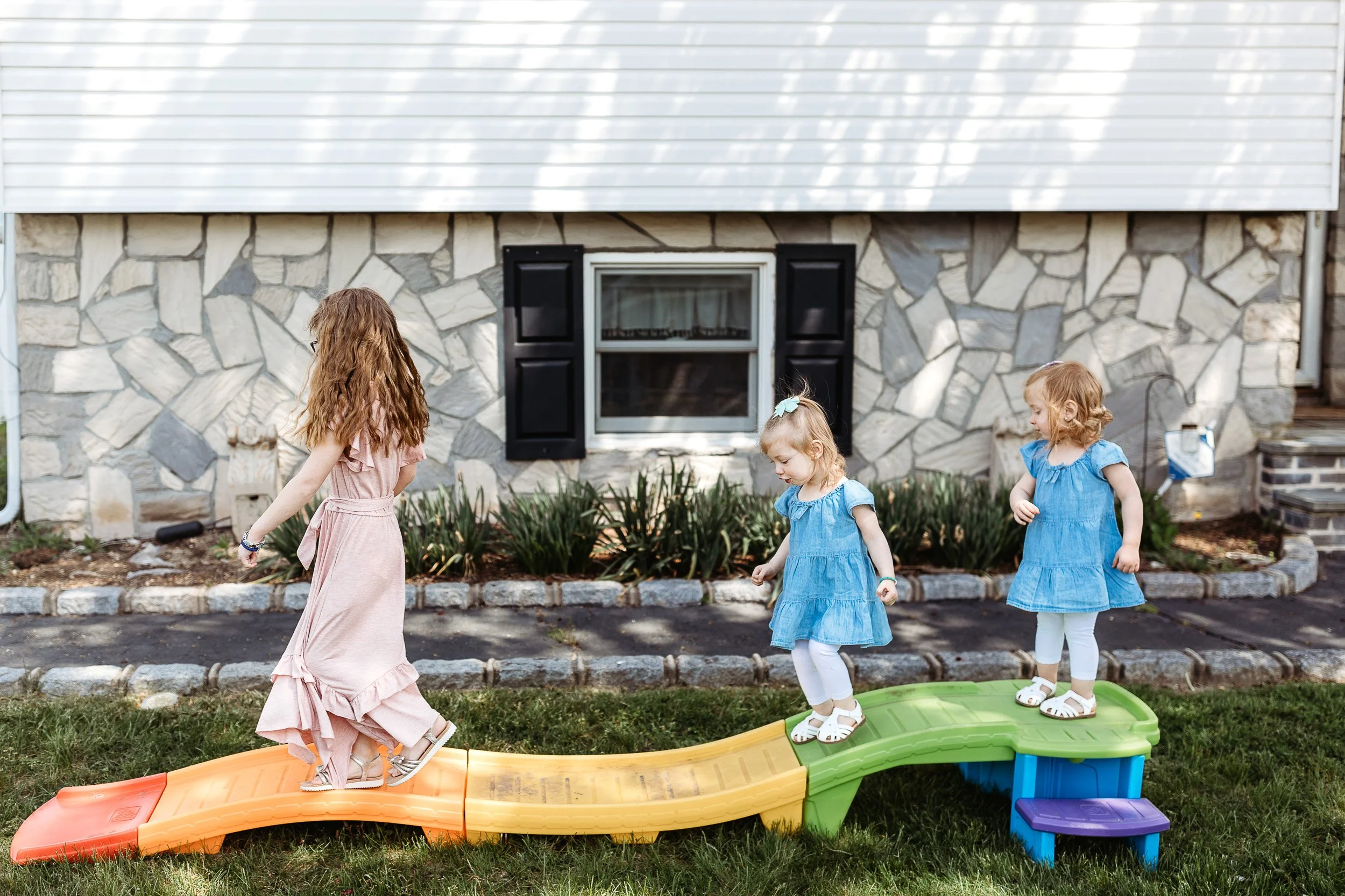 children balancing on the little tikes plastic roller coaster in front of their home single file for family photos in Jacksonville area